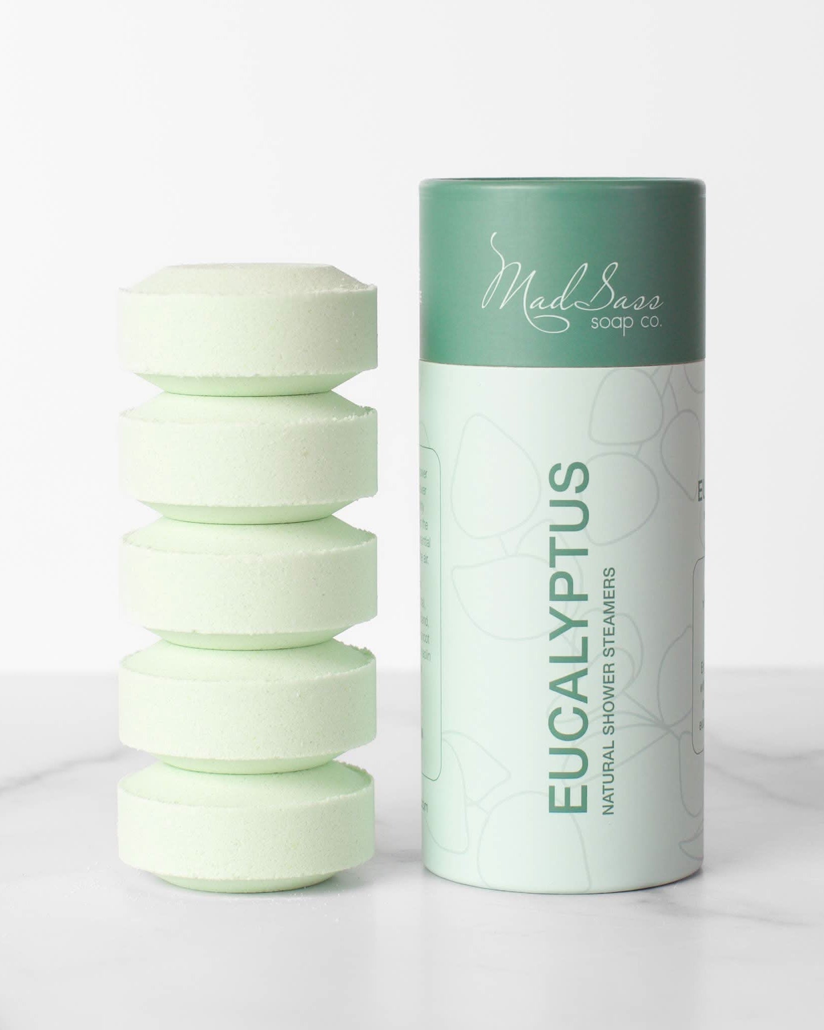 Stacked green eucalyptus shower steamer tablets next to packaging