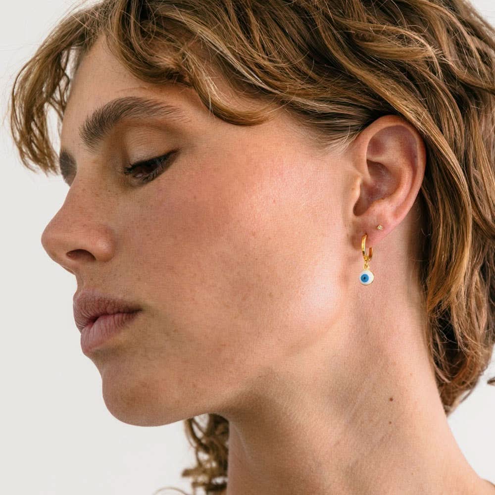 Woman wearing Gold earring with glass evil eye charm white with blue eye