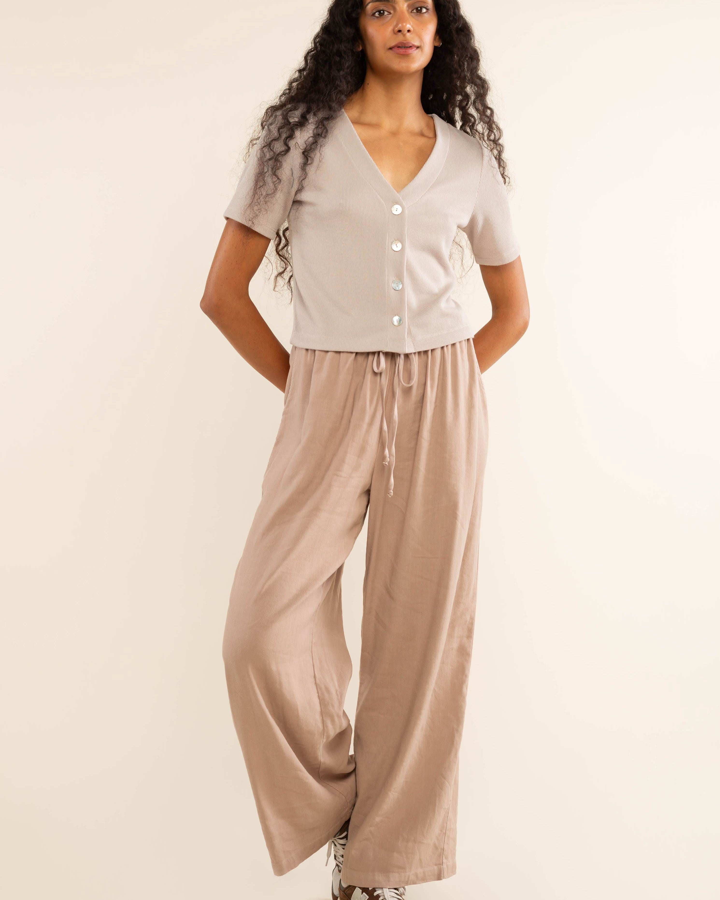 Woman wearing oat colored, ribbed, button down, short sleeve blouse top and beige pants
