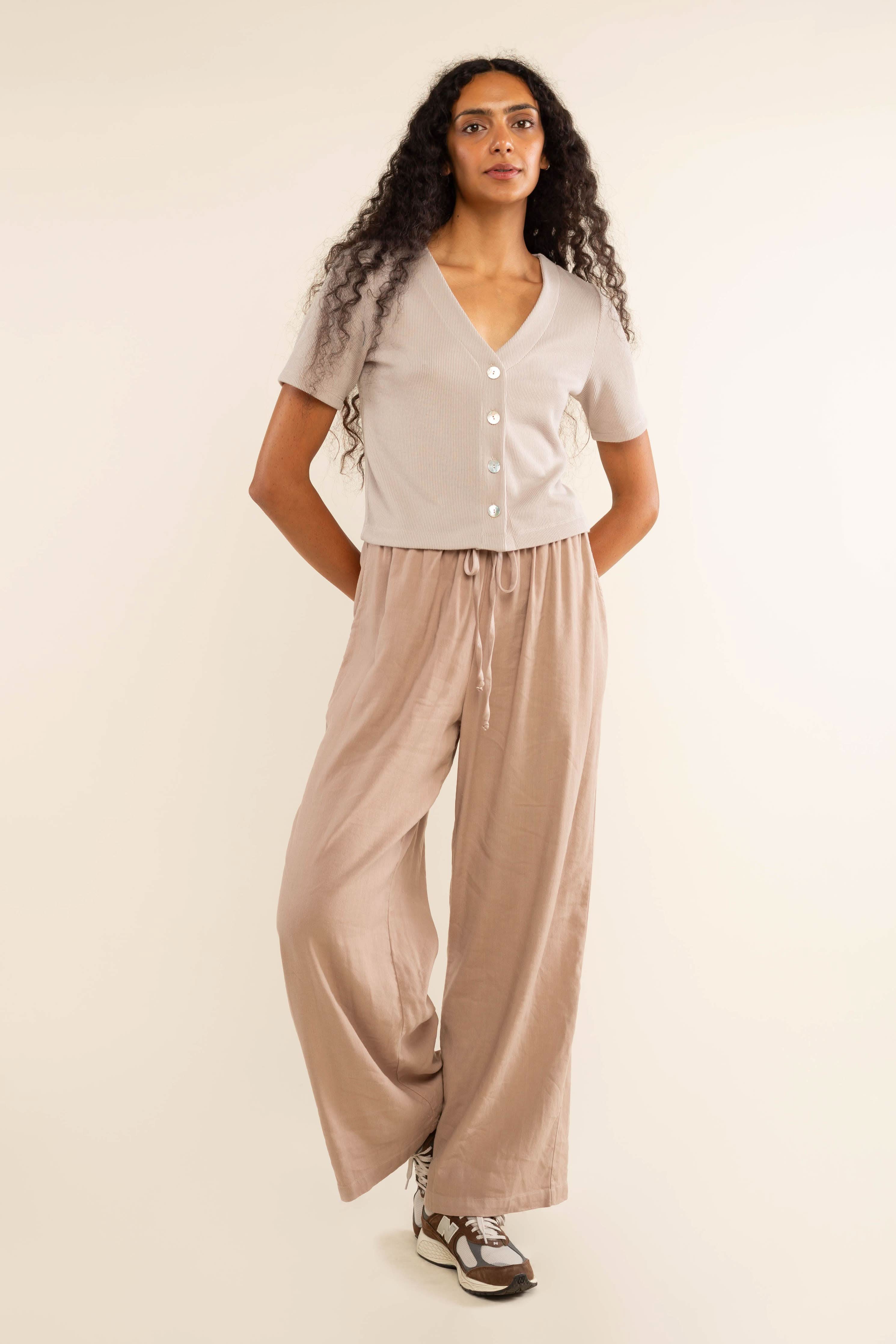 Woman wearing oat colored, ribbed, button down, short sleeve blouse top and beige pants