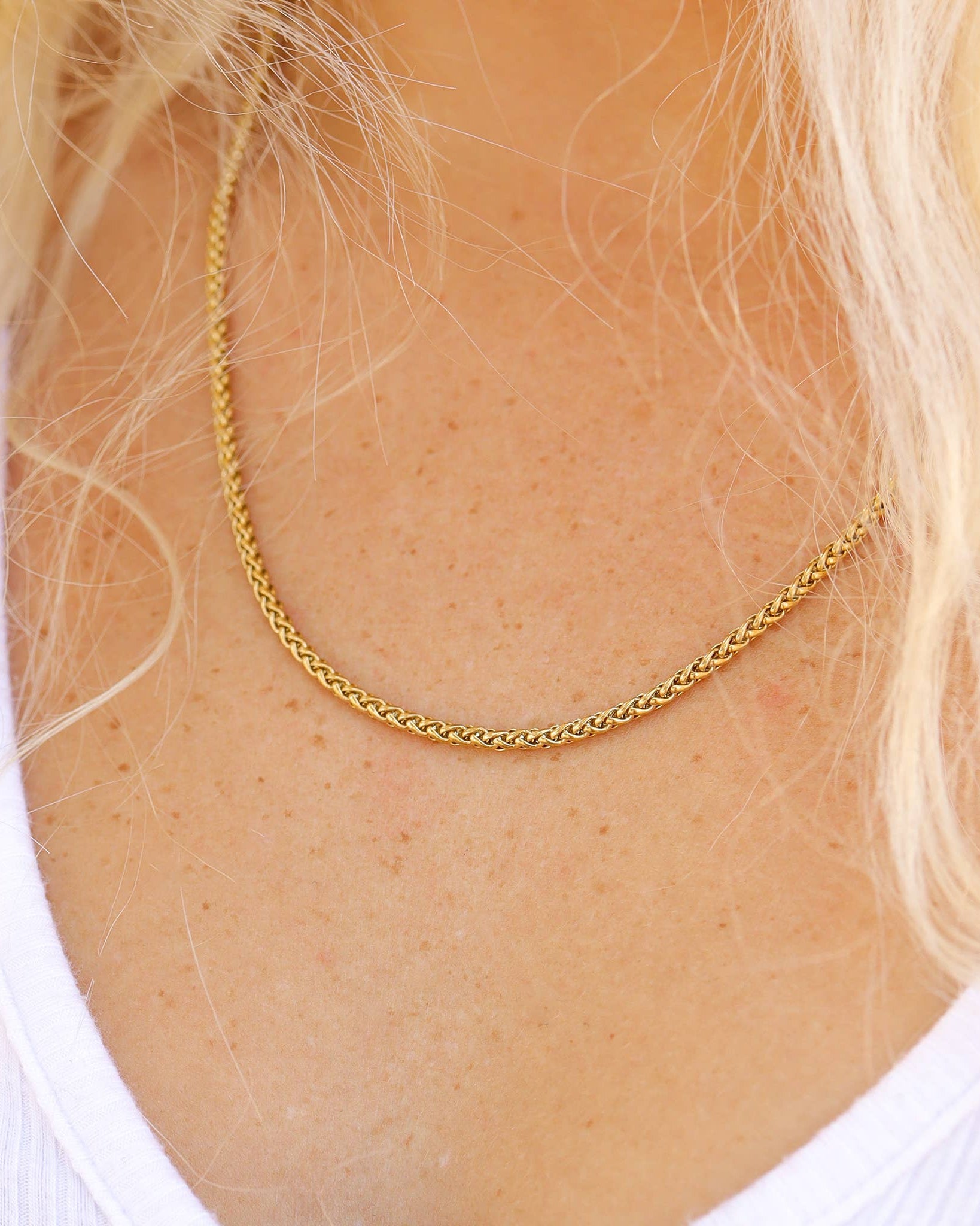 Gold chain necklace on a person with blonde hair and a white shirt.