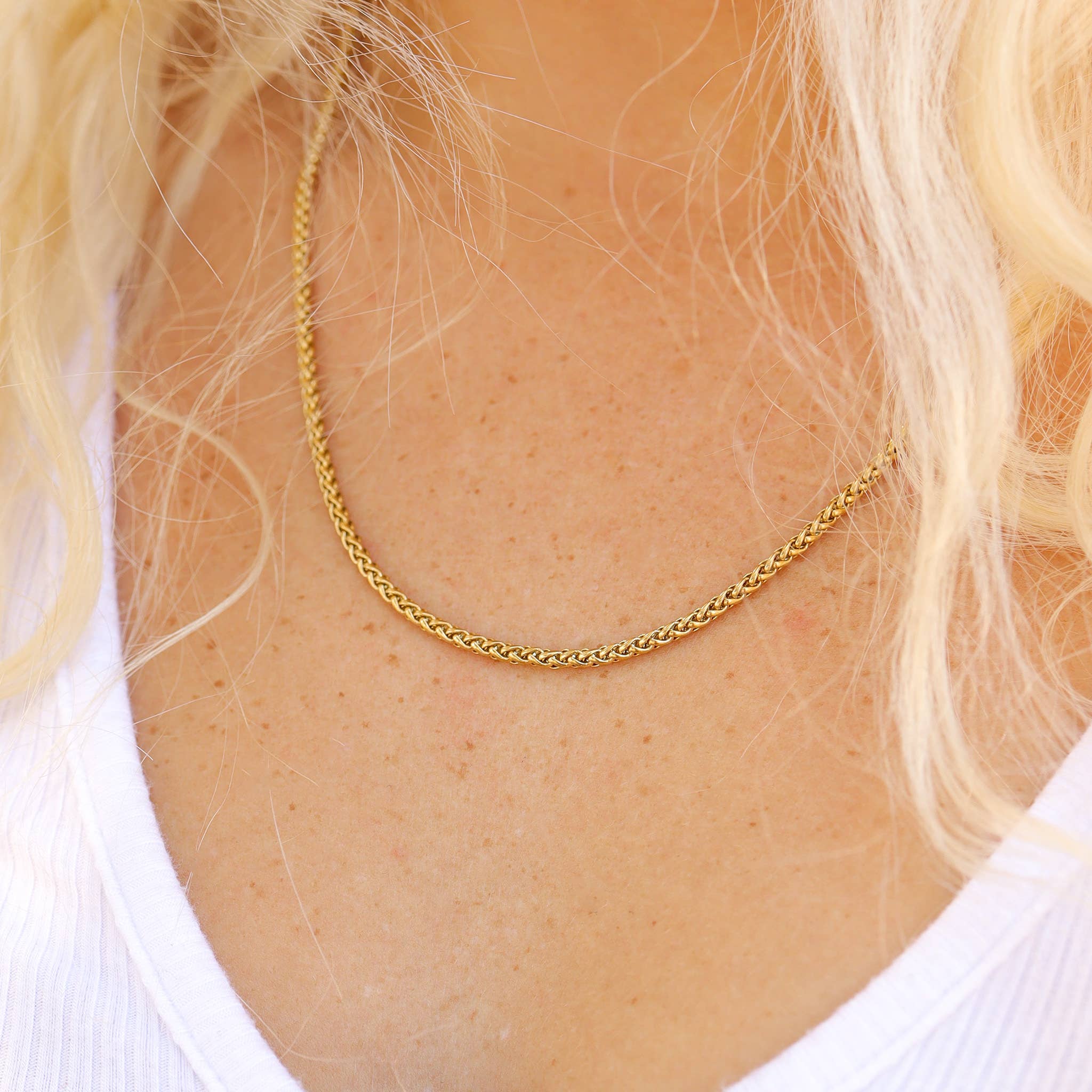 Gold chain necklace on a person with blonde hair and a white shirt.