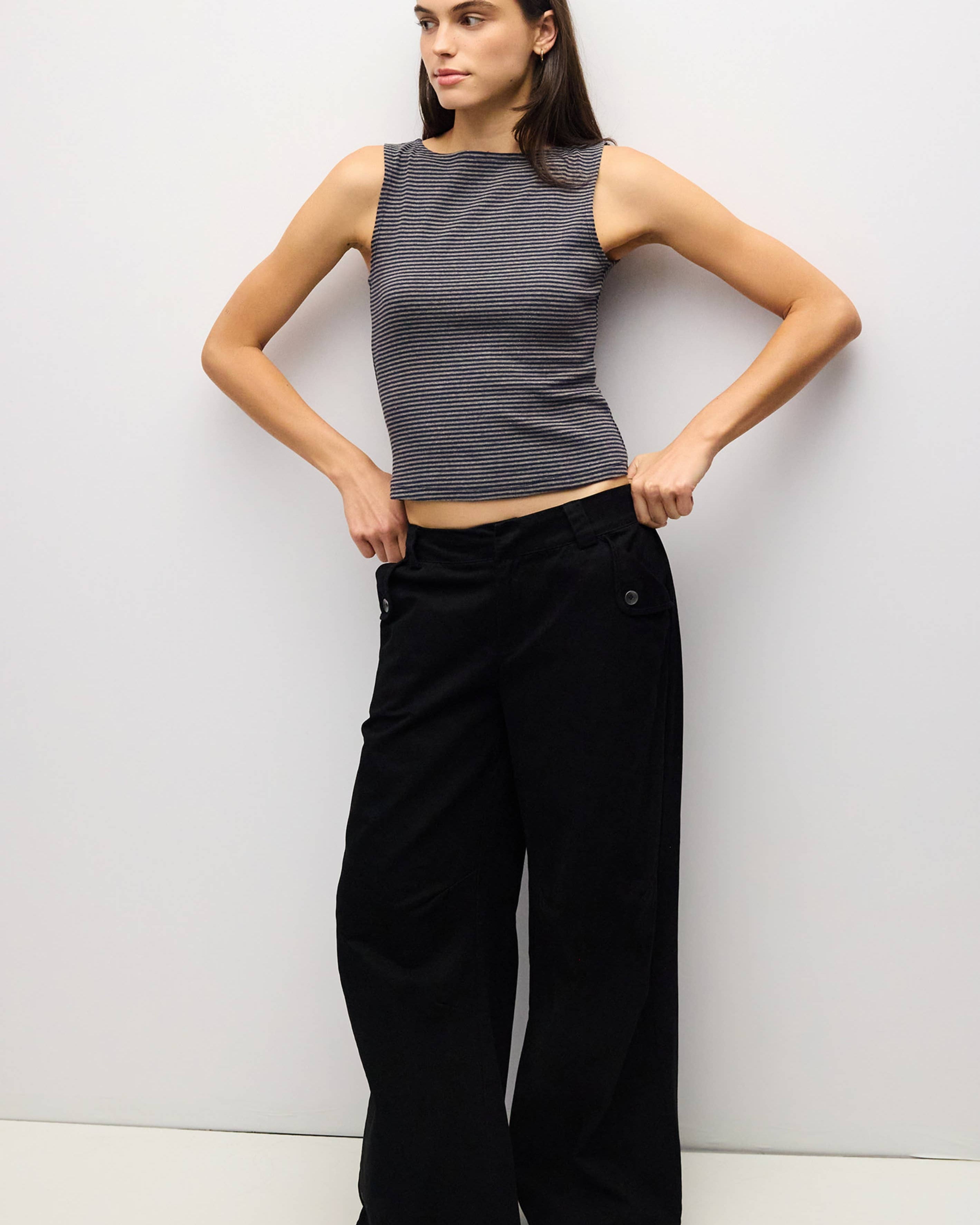 A woman modeling a sleeveless dark gray ribbed crop top and black wide-leg pants against a plain light gray studio background.