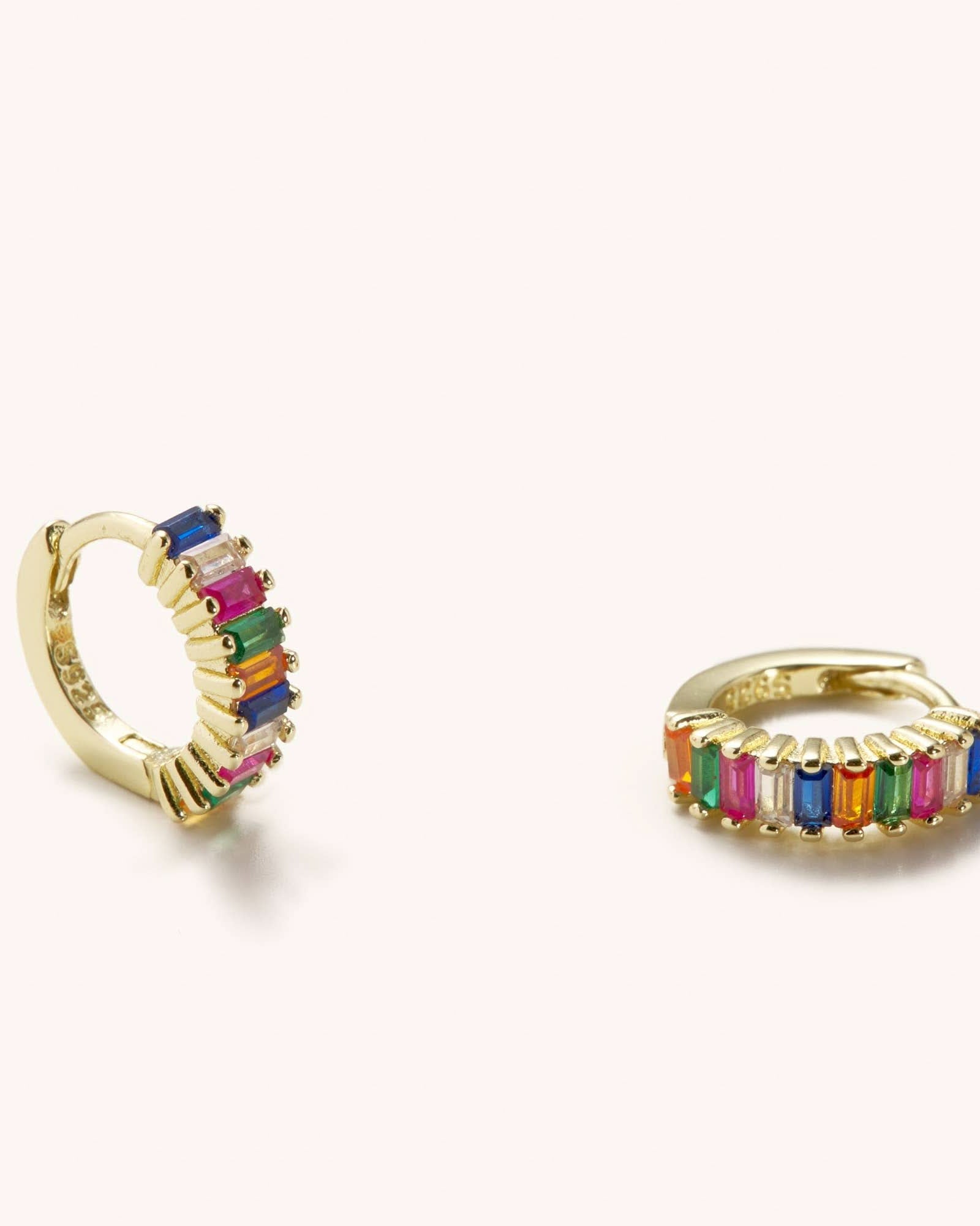 Small sized rainbow gem huggie earrings laying against a white background