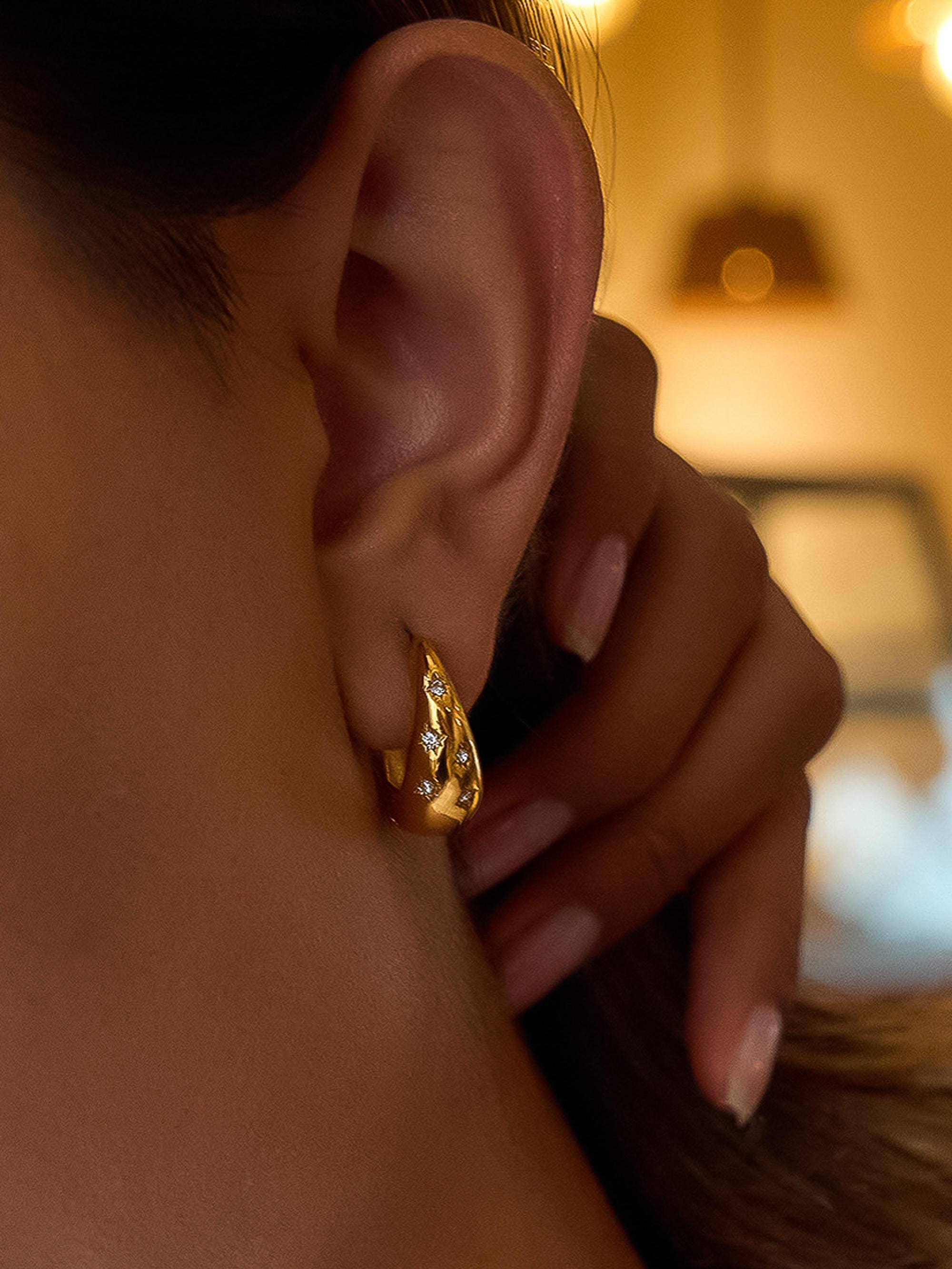 Close-up of an ear wearing a gold earring with a blurred background