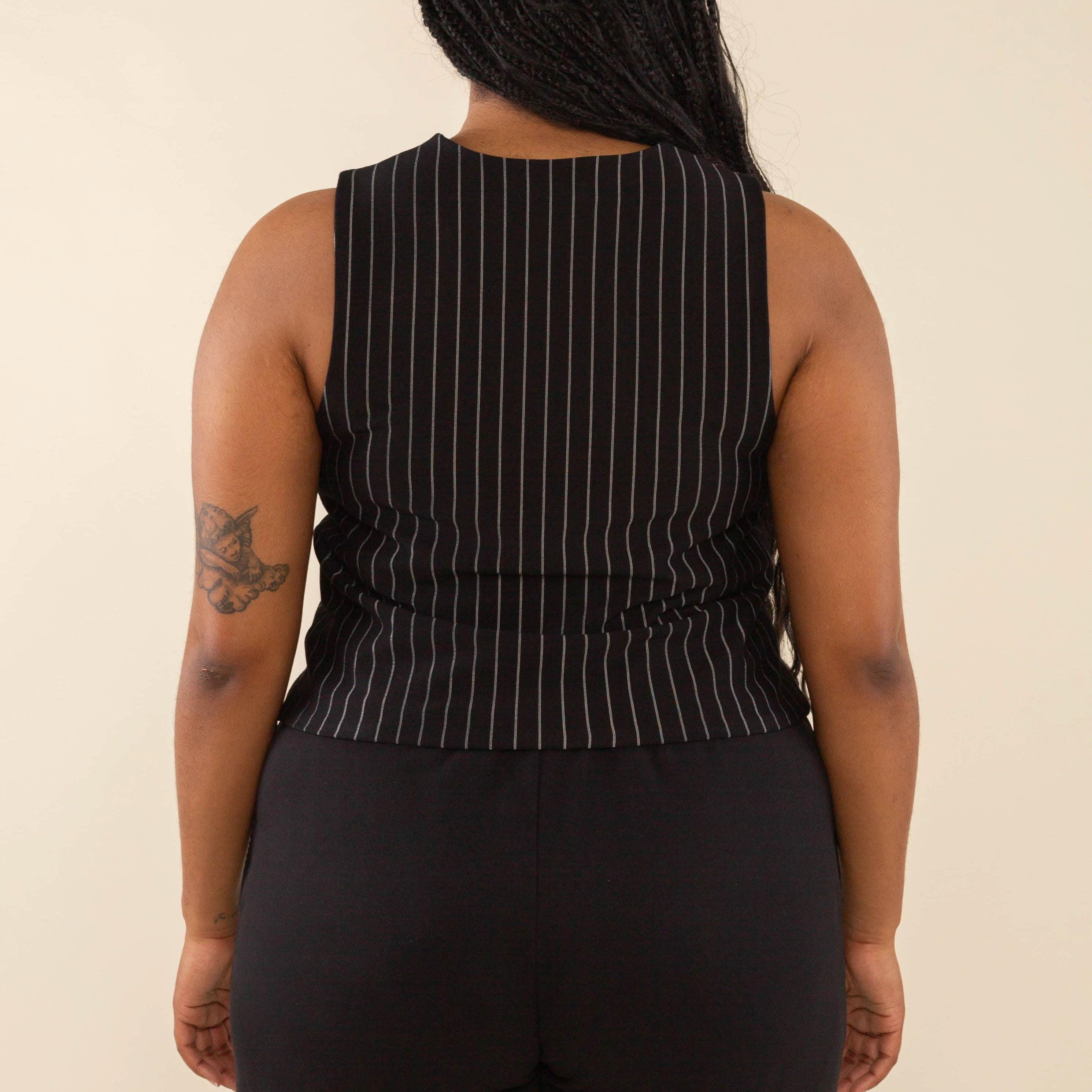 Woman turned away from the camera wearing black high neck vest with cream pinstripes. Vest has black buttons all the way down