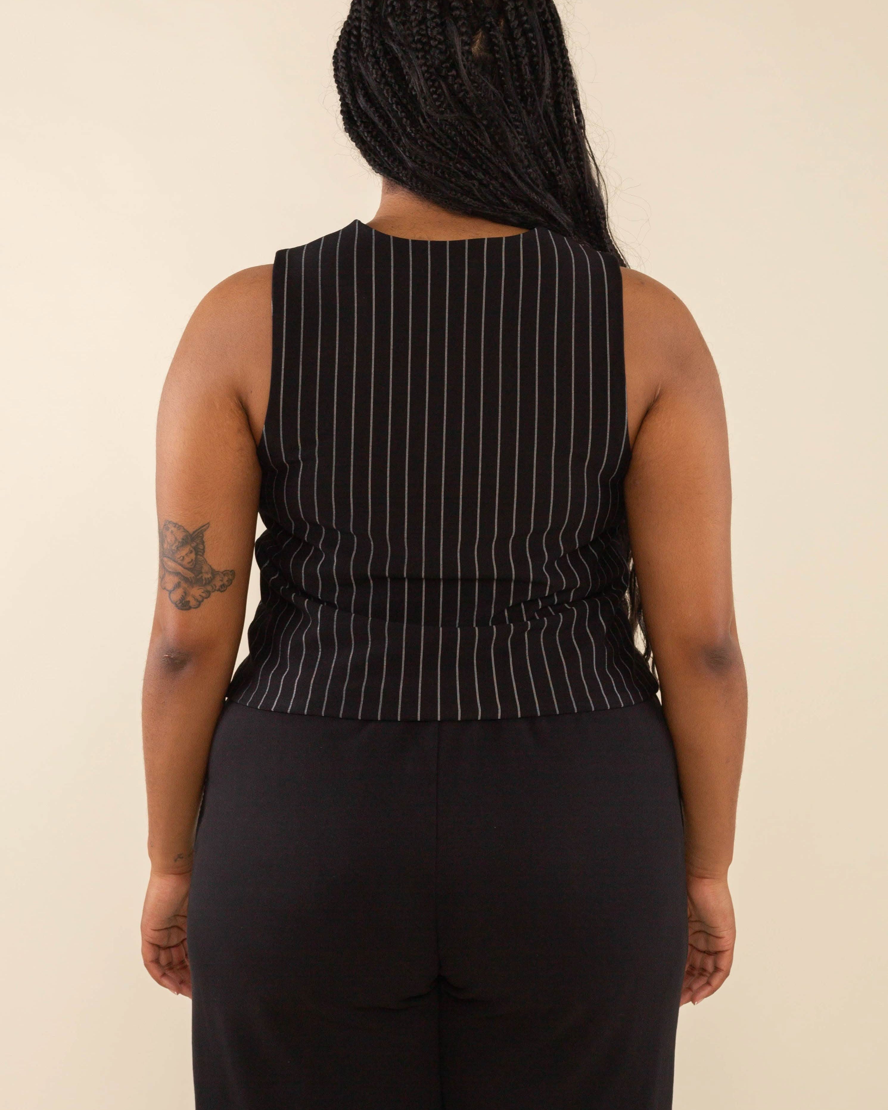 Woman turned away from the camera wearing black high neck vest with cream pinstripes. Vest has black buttons all the way down