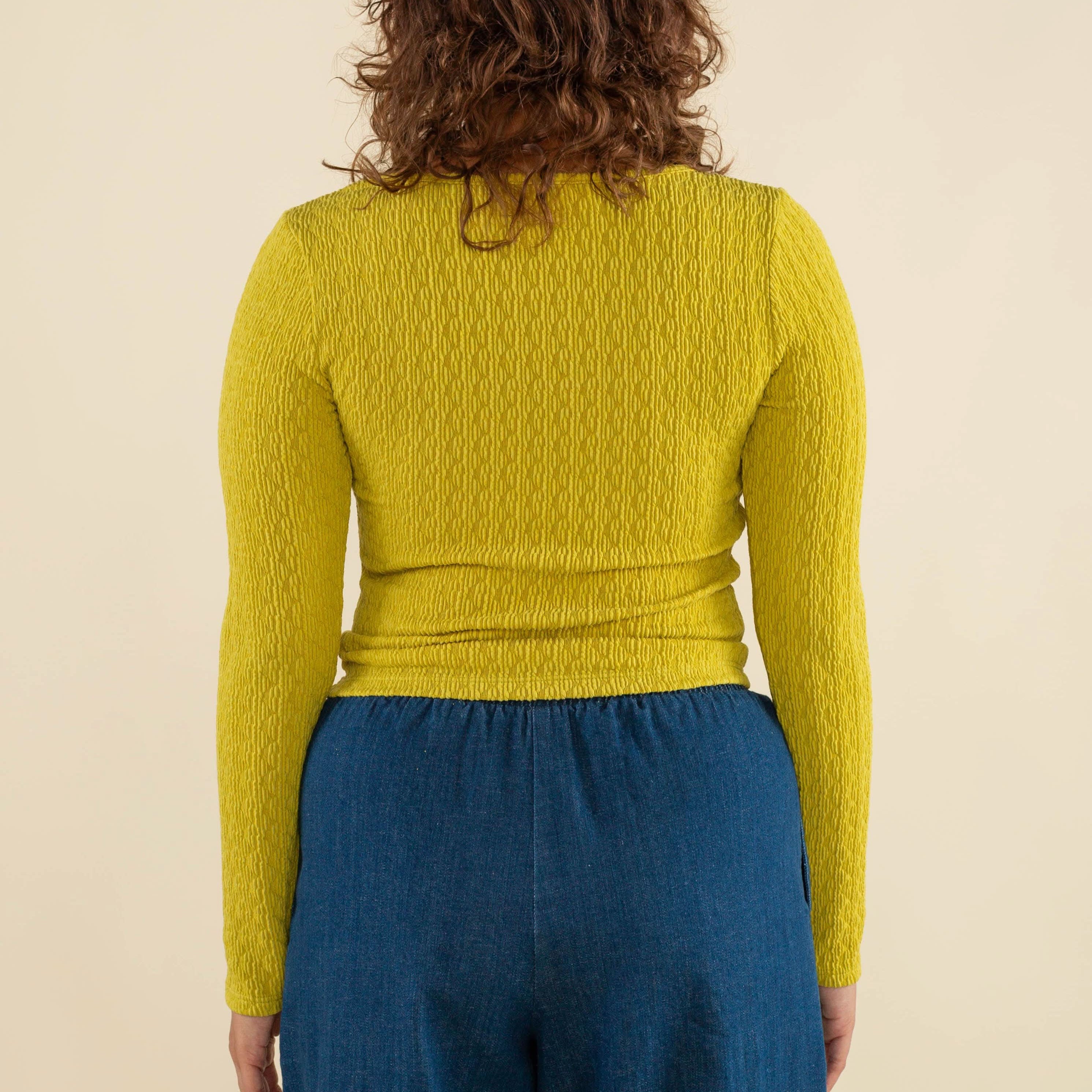 Woman wearing chartreuse, square neck line, textured, long sleeve top and jeans