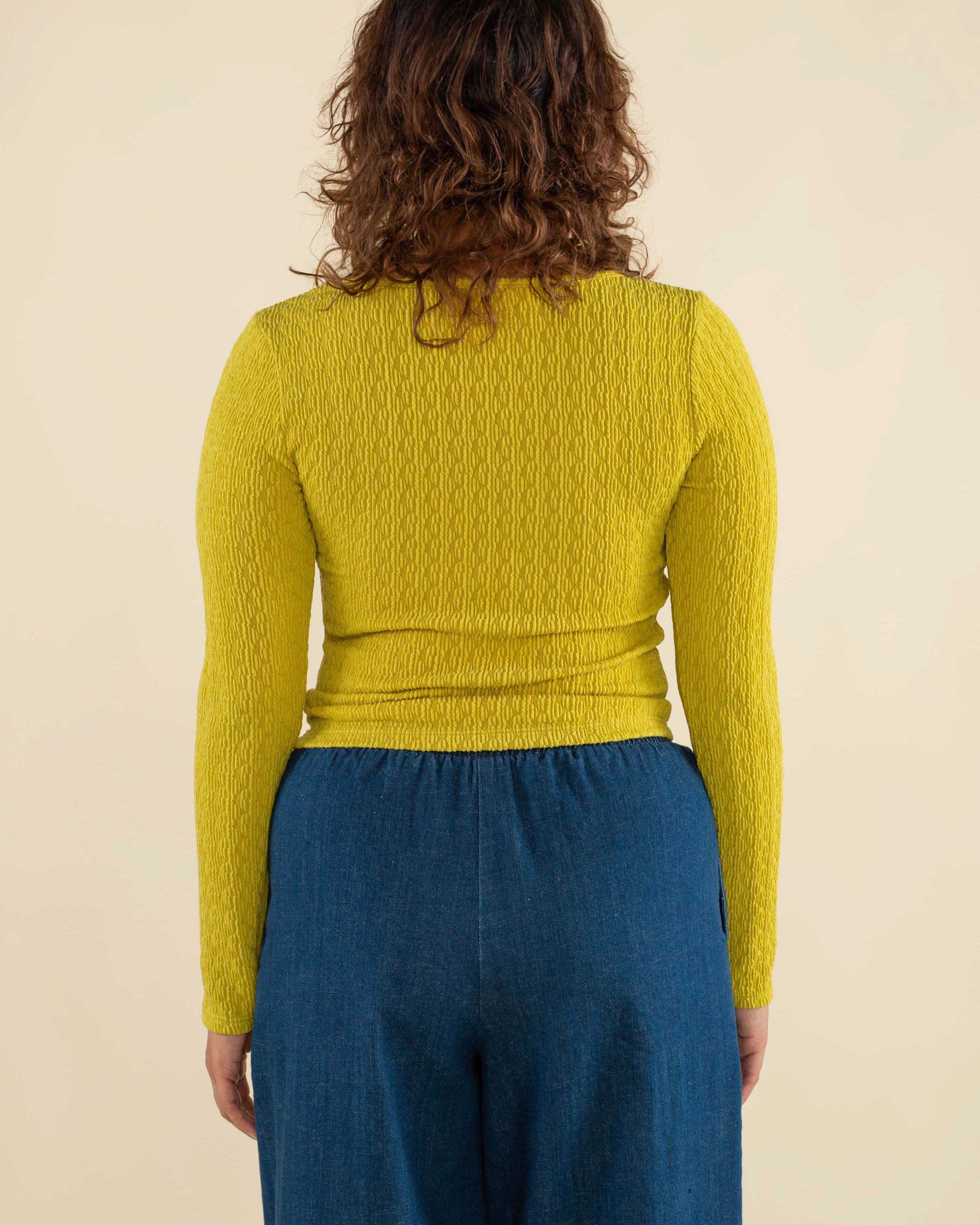 Woman wearing chartreuse, square neck line, textured, long sleeve top and jeans