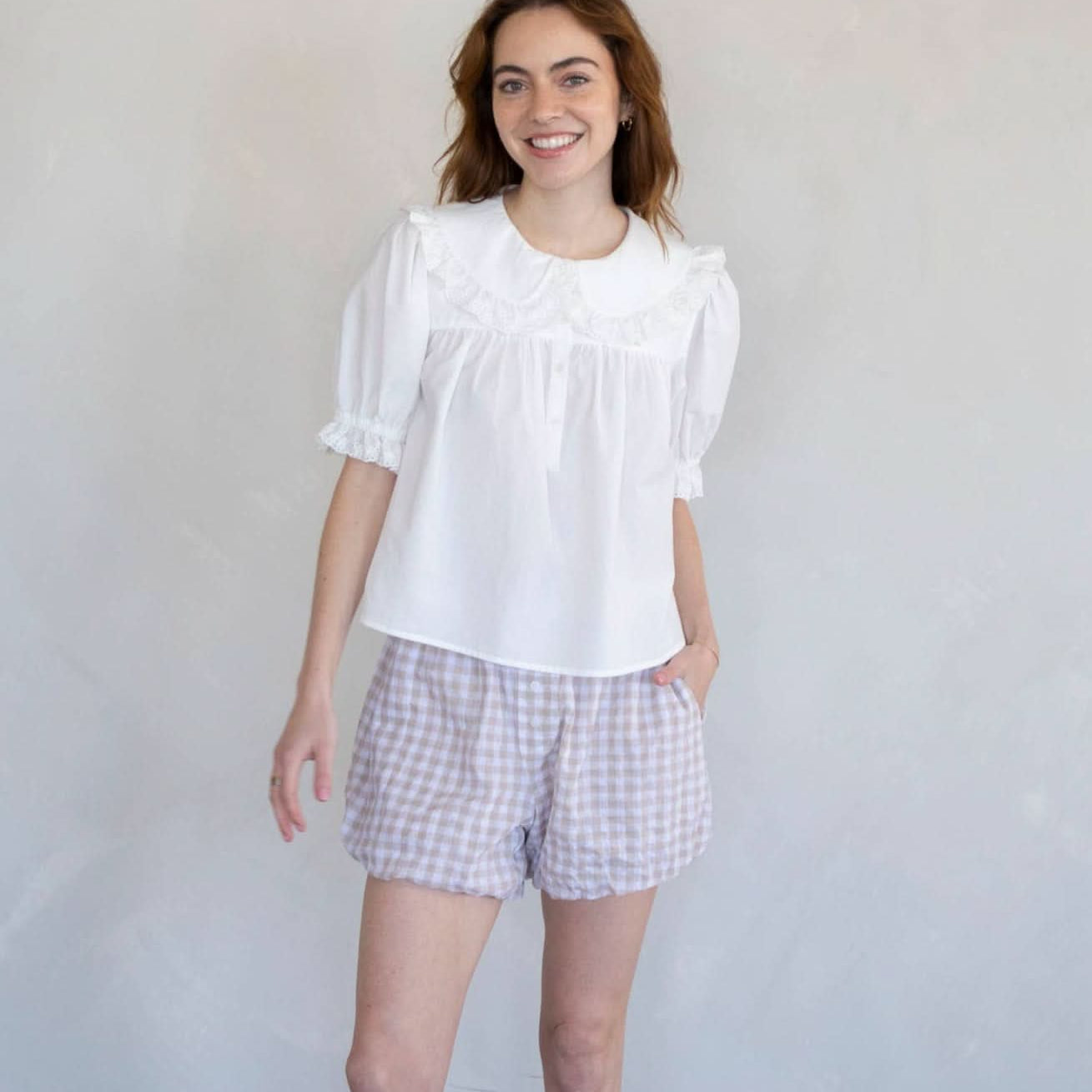 Woman wearing white half button dreamy sweetheart blouse and plaid shorts