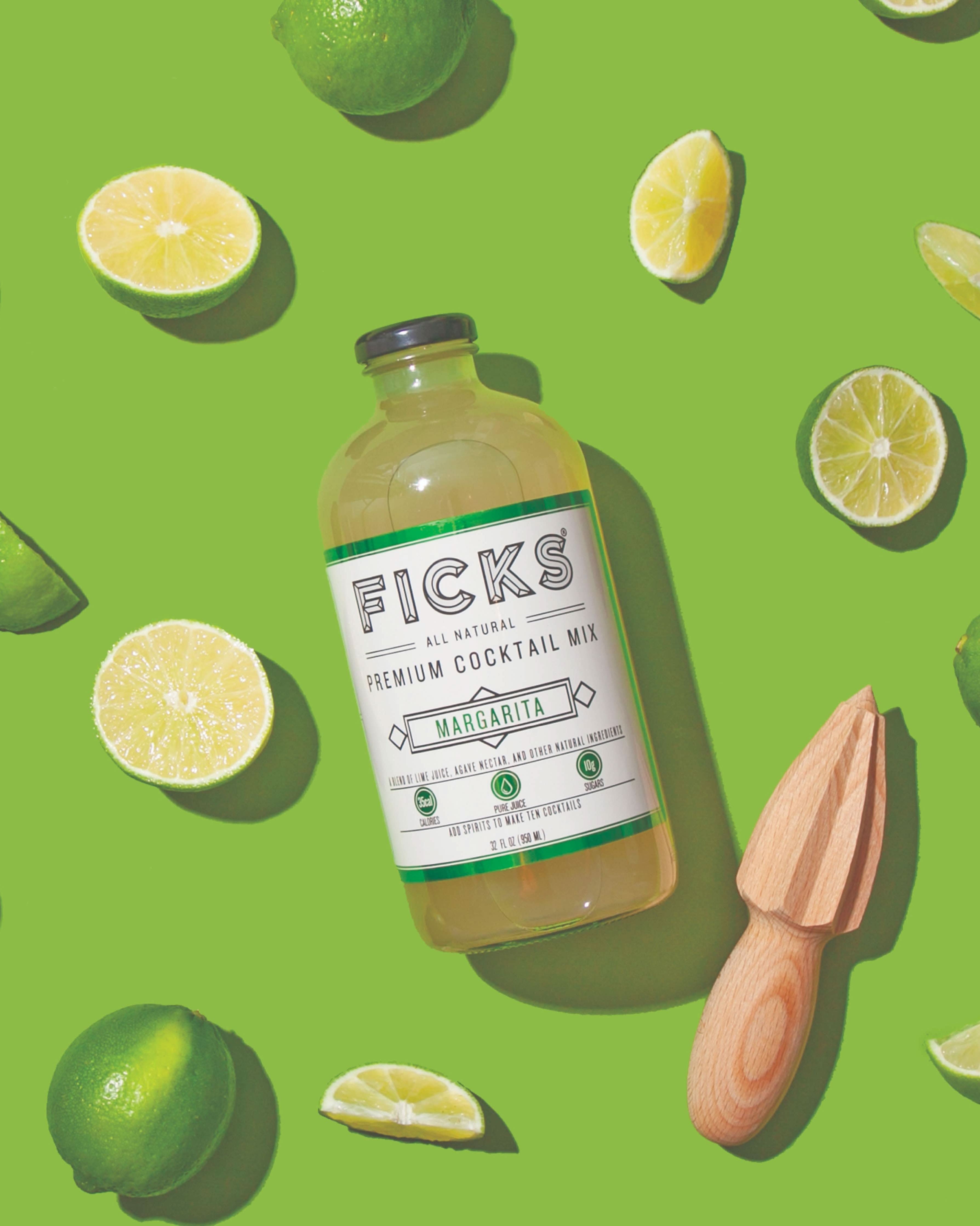 Glass cocktail bottle laying flat on green surface surrounded slices limes