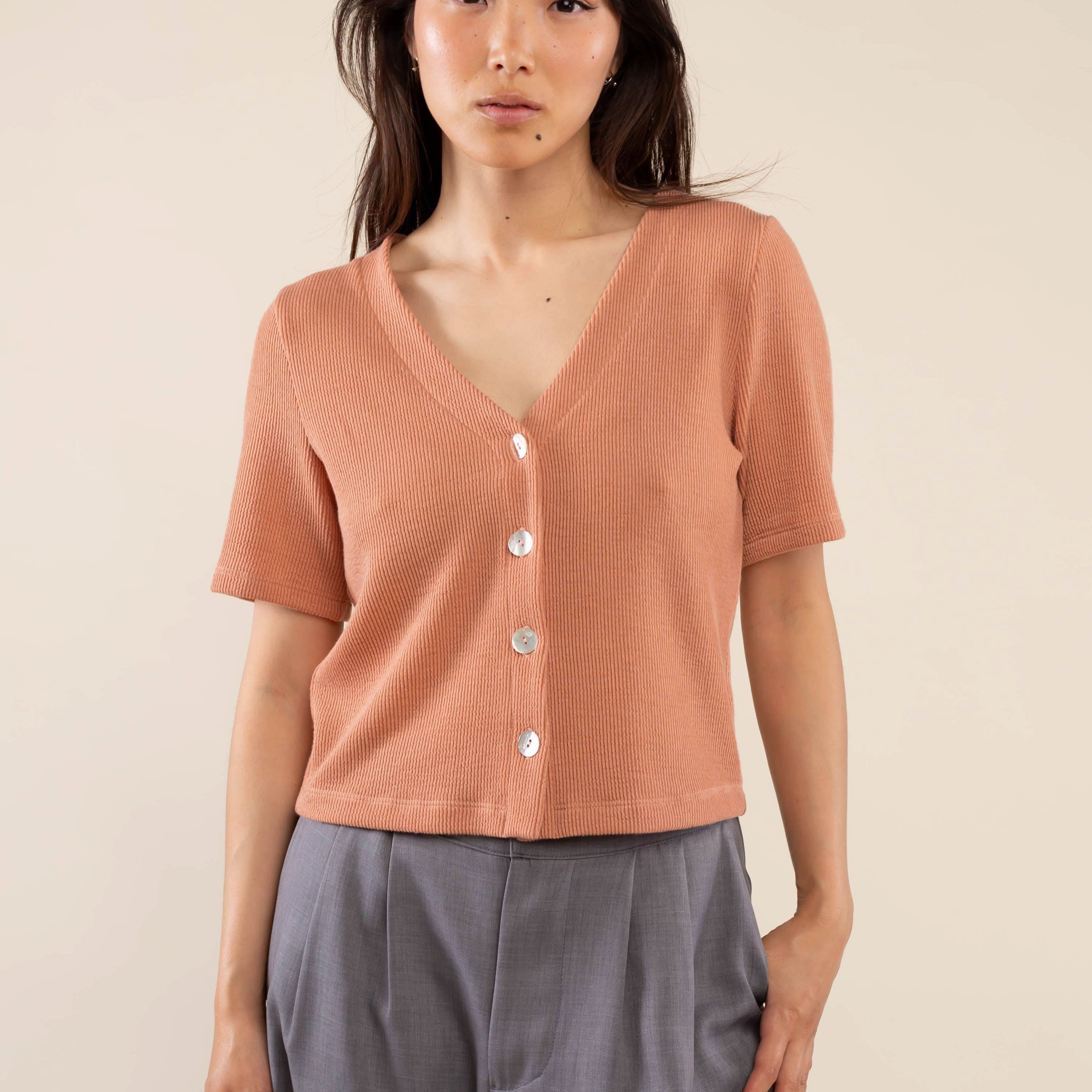 Woman wearing brick colored, ribbed, button down, short sleeve blouse top and grey pants