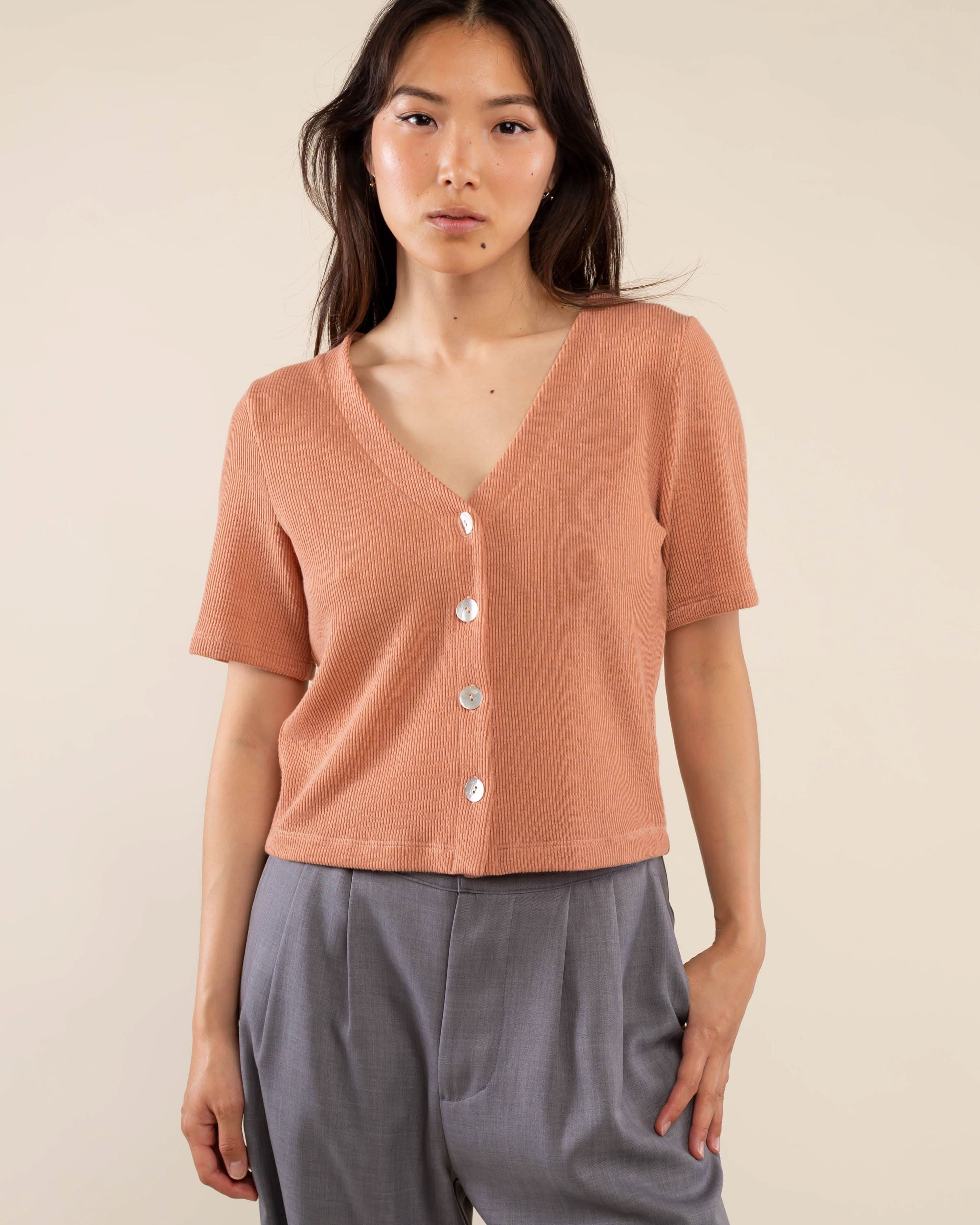 Woman wearing brick colored, ribbed, button down, short sleeve blouse top and grey pants
