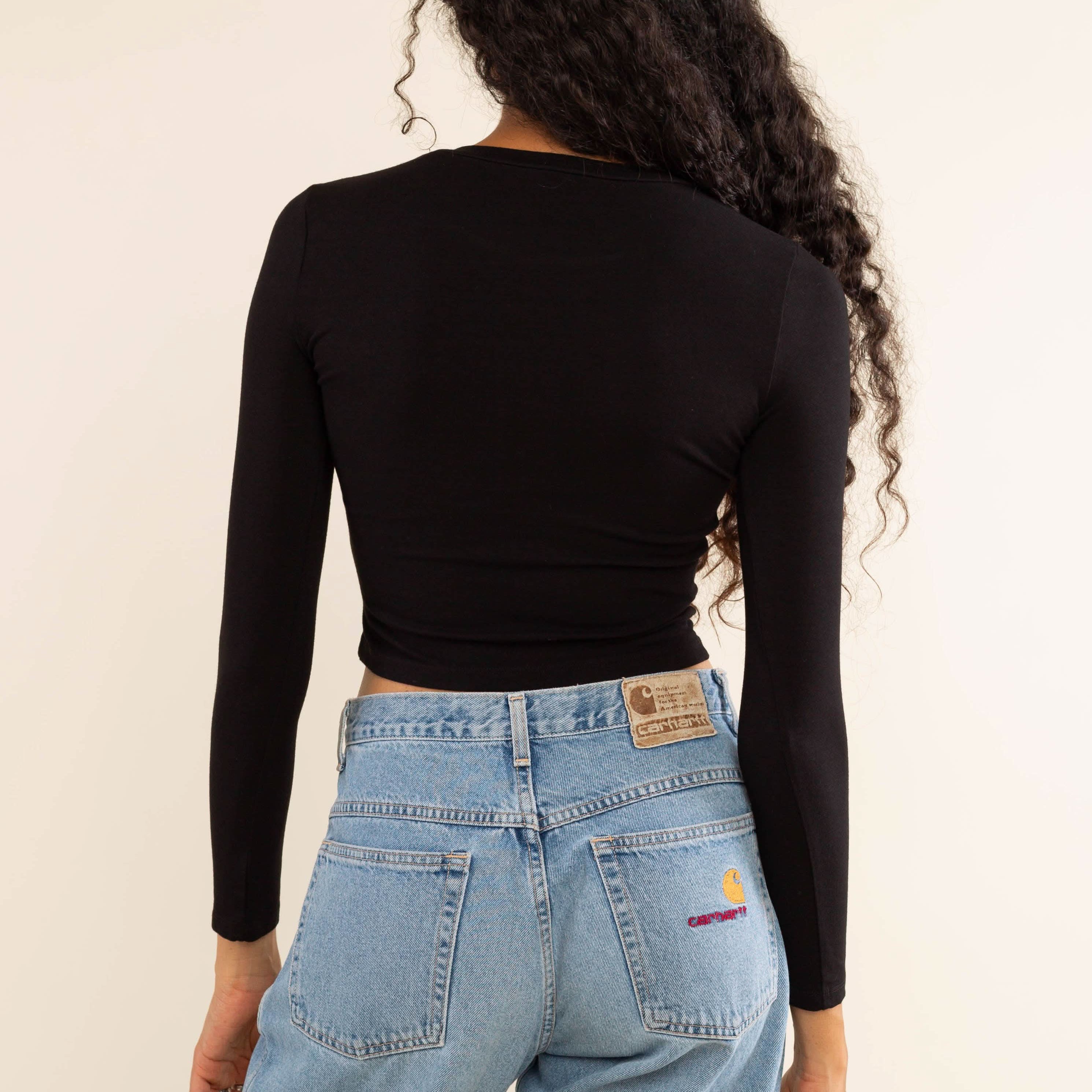 Woman wearing white, long sleeve, tight, crew neck, top with blue carhartt jeans