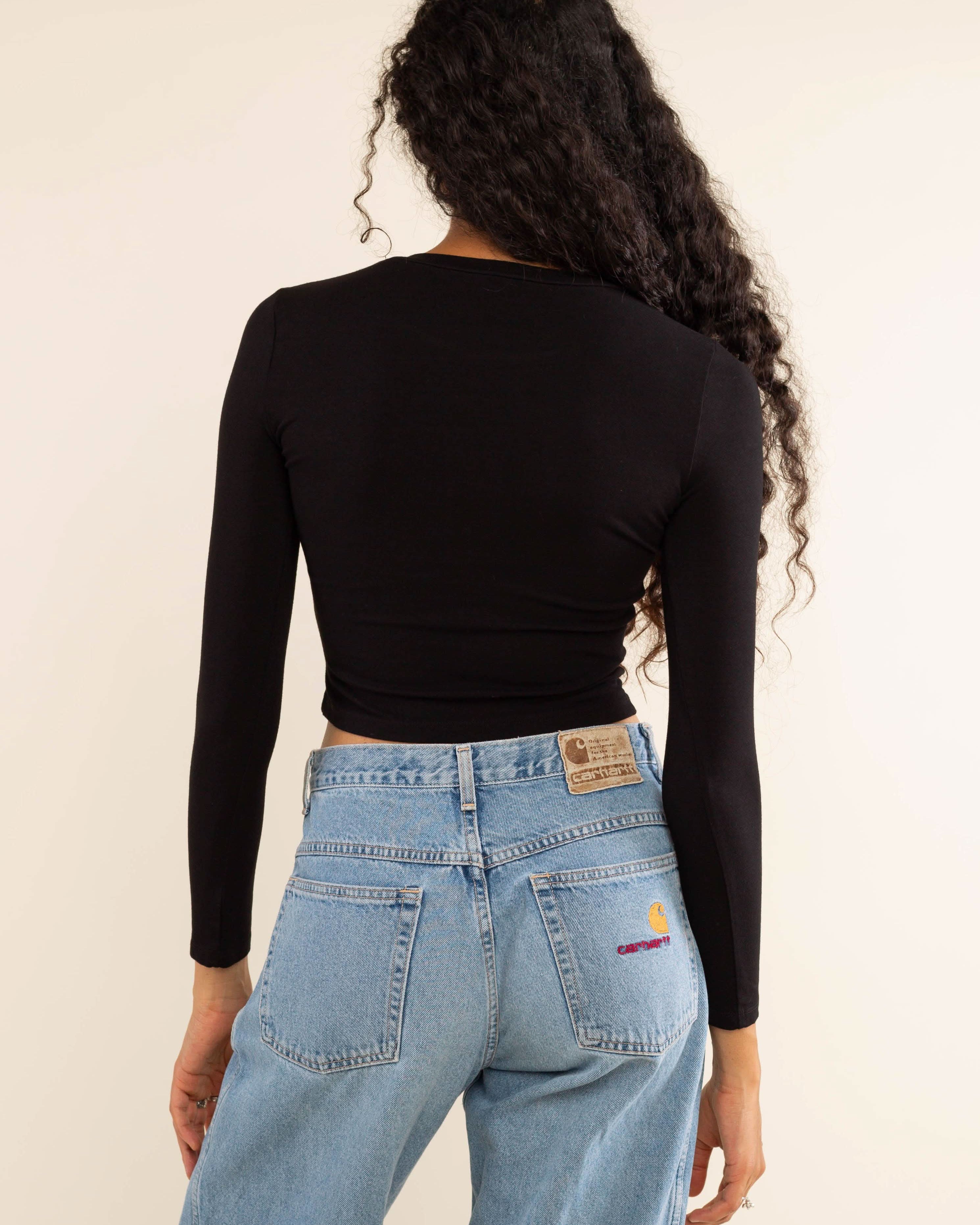 Woman wearing white, long sleeve, tight, crew neck, top with blue carhartt jeans
