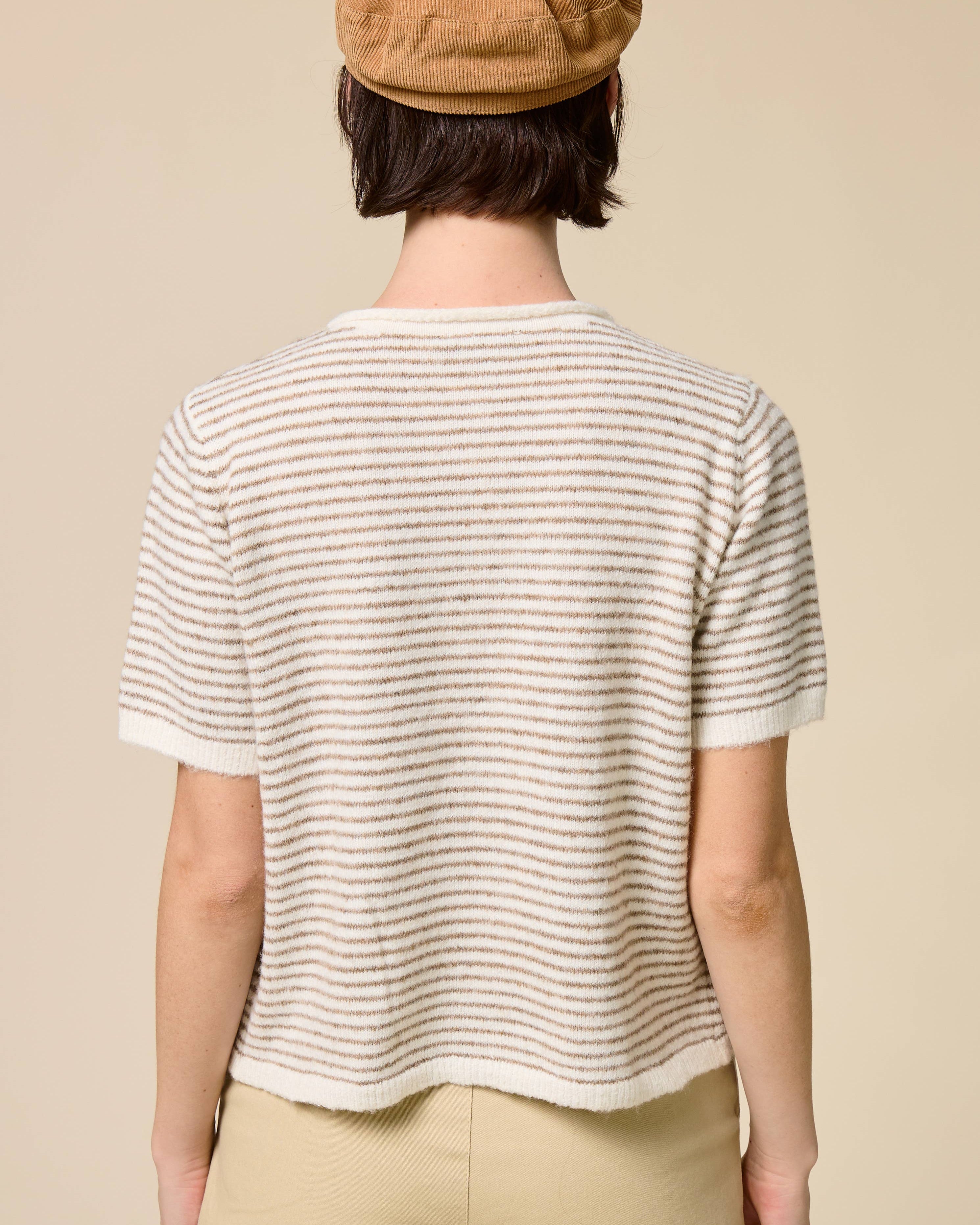 Person wearing a striped shirt and beige cap on a plain background