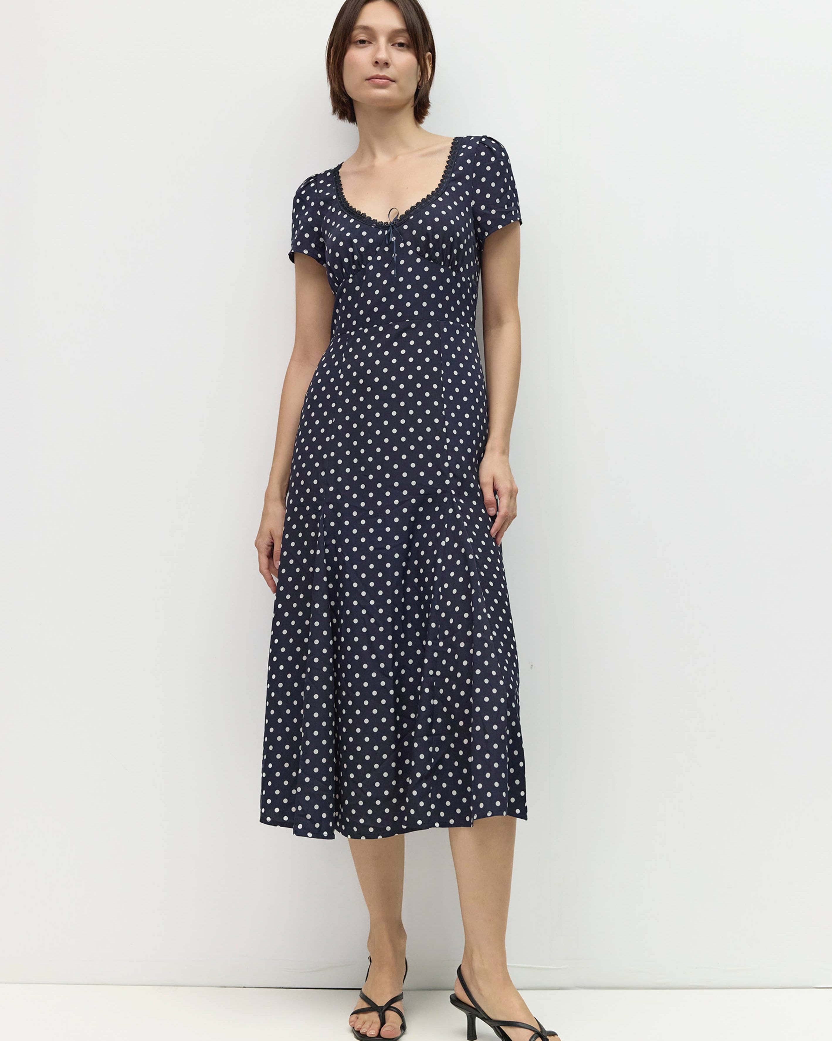 Woman wearing a navy dress with white polka dots against a white background