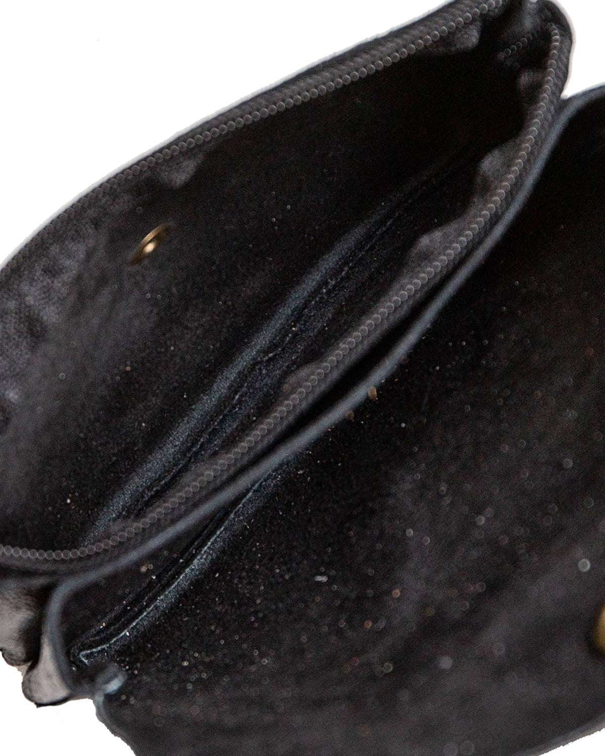 Close-up of the interior of a black fabric pouch or clutch bag, showing the lining, zipper edge, and a small brass grommet on a white background.