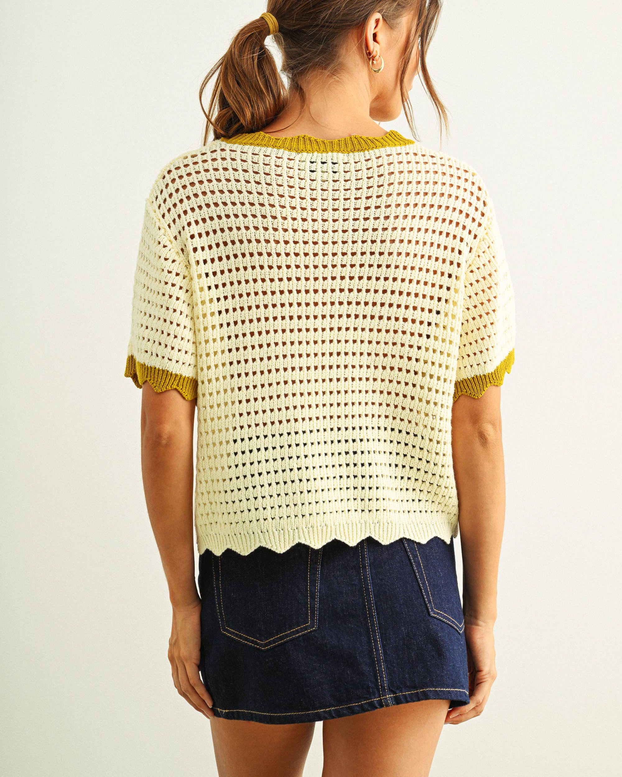 Woman wearing a white crochet top and denim skirt on a plain background