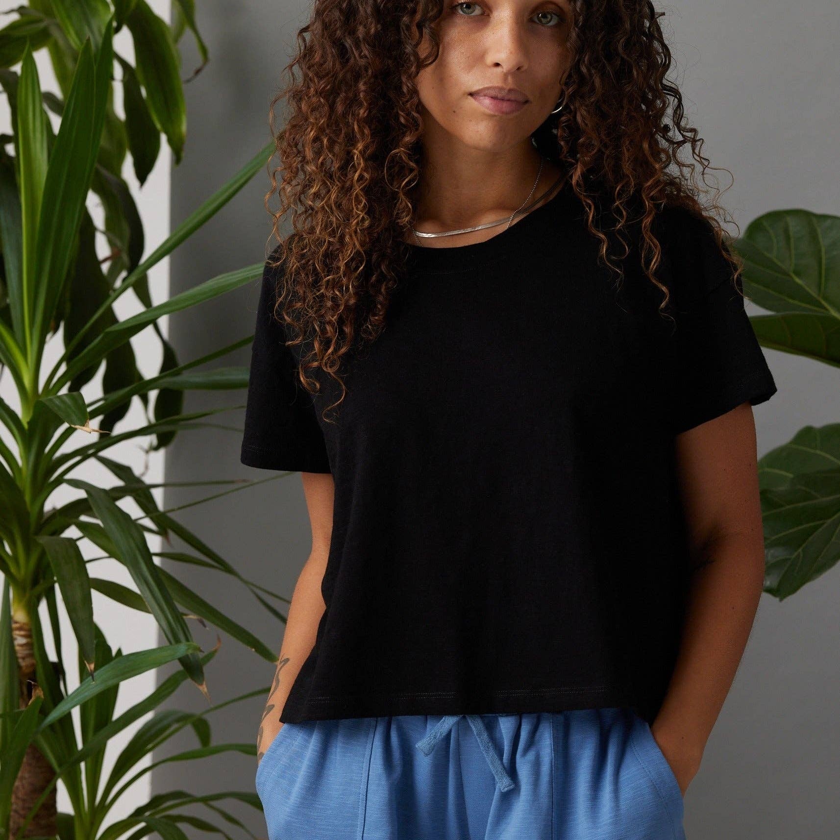 Woman wearing a black t-shirt and blue pants standing in front of green plants.