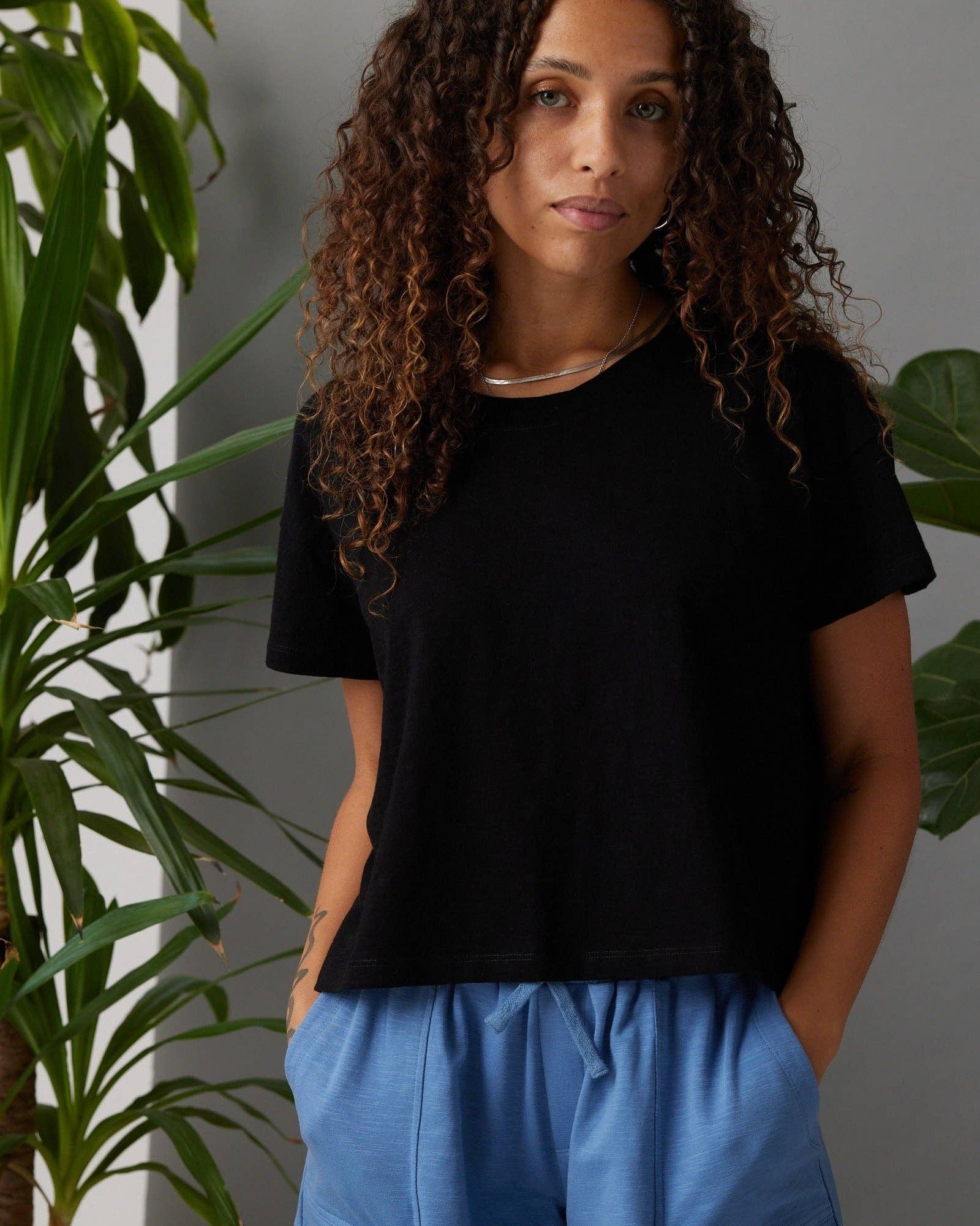 Woman wearing a black t-shirt and blue pants standing in front of green plants.