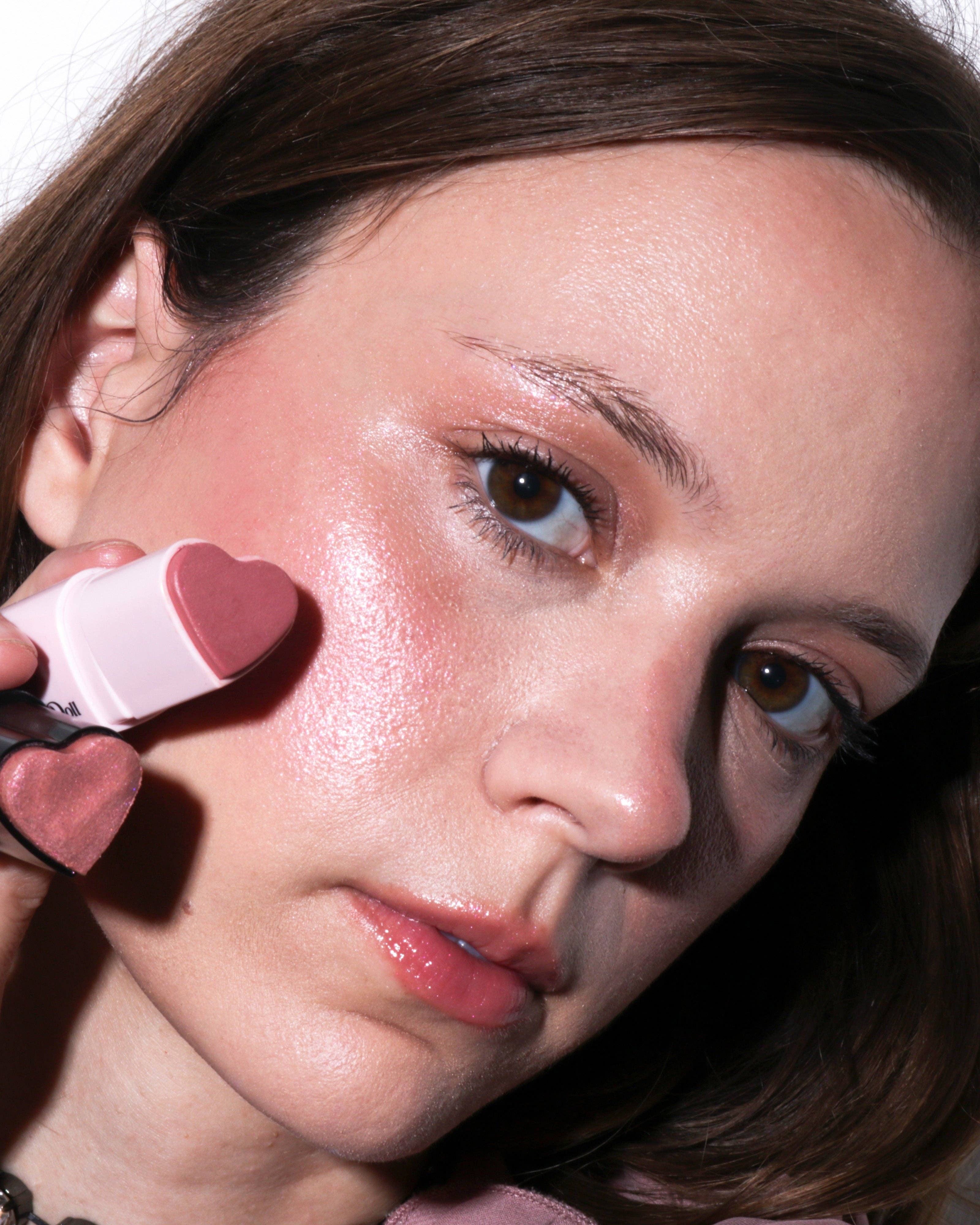 Woman applying pink makeup with a heart-shaped applicator.