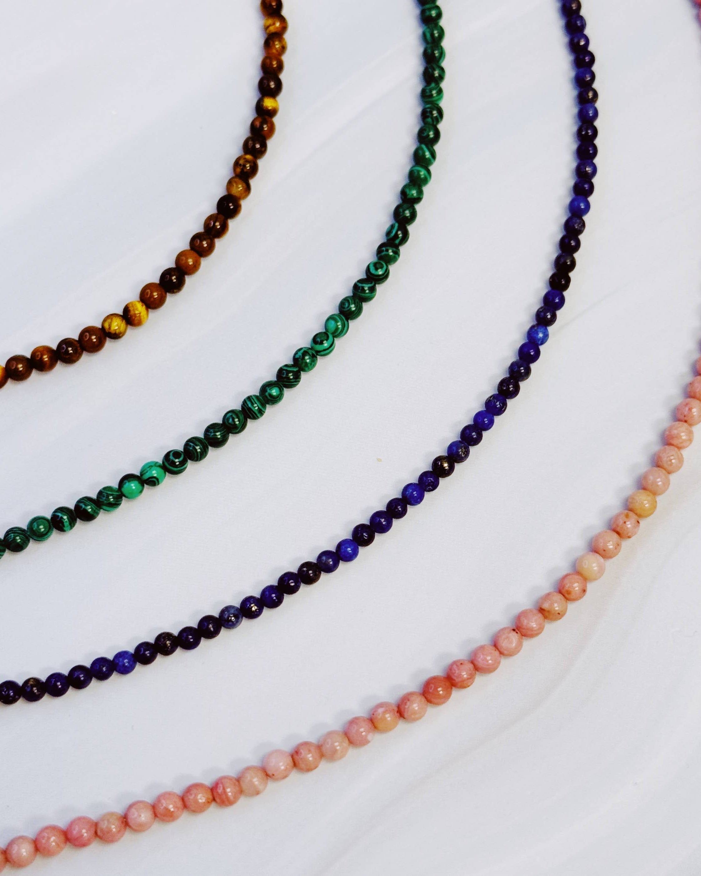 Four beaded necklaces in different colors on a white background