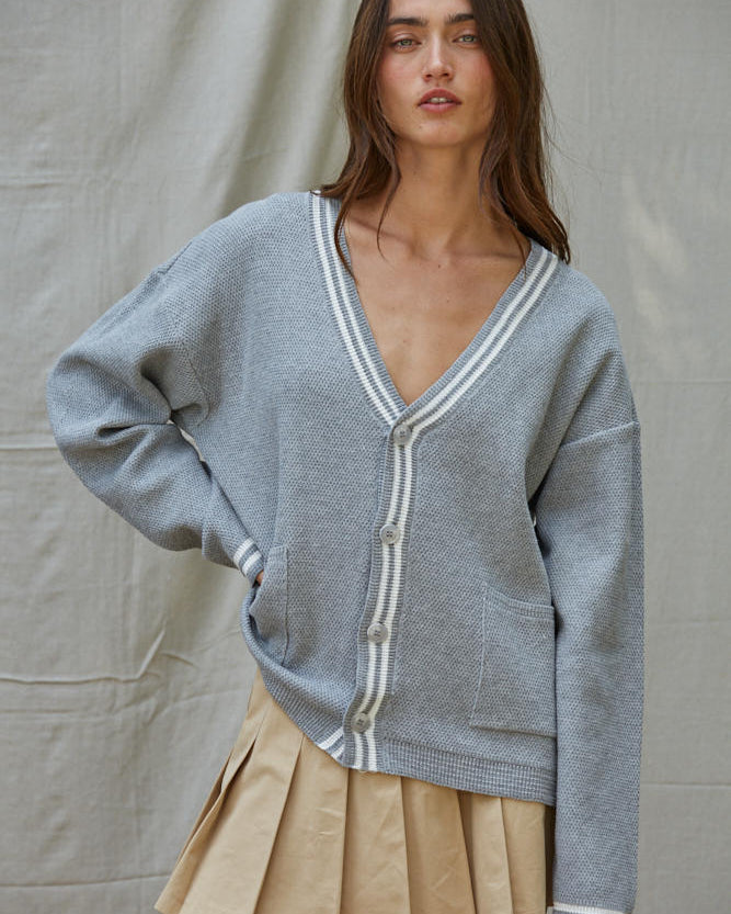 Woman wearing a gray cardigan with white trim over a beige skirt