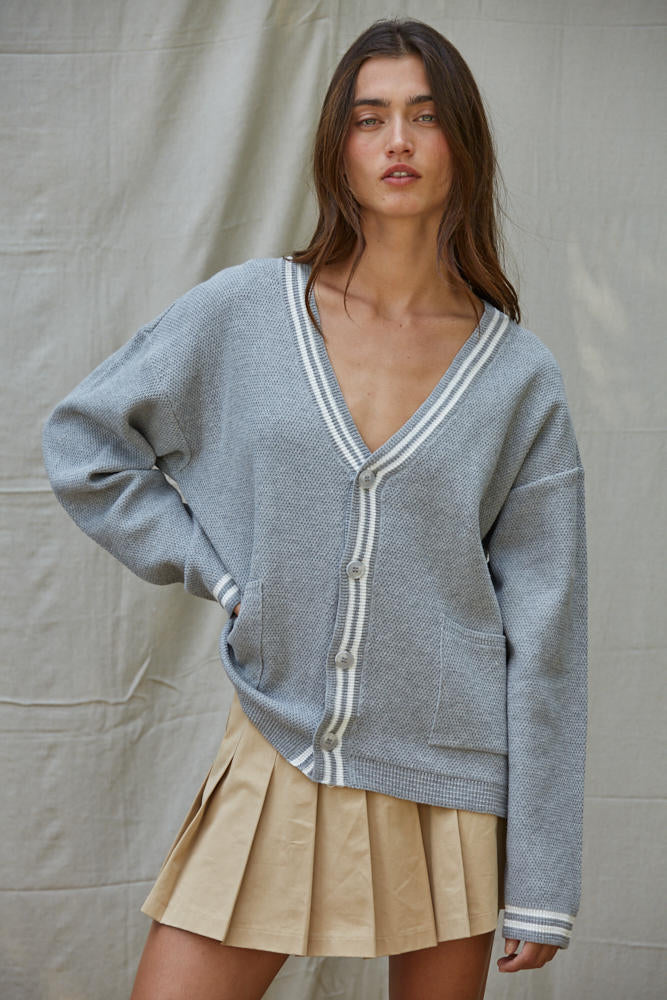 Woman wearing a gray cardigan with white trim over a beige skirt