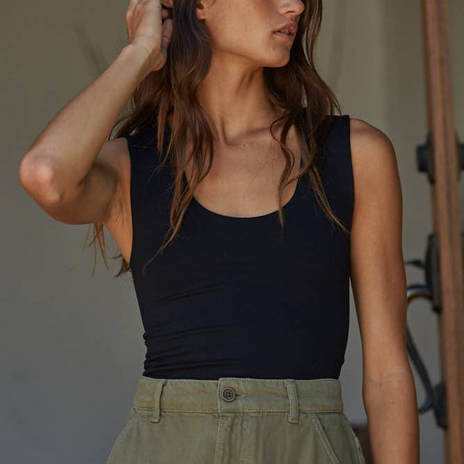 Woman wearing a black sleeveless top and green pants indoors.