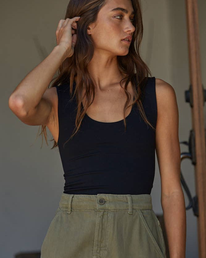 Woman wearing a black sleeveless top and green pants indoors.