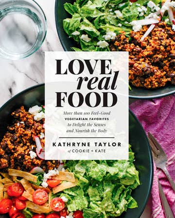 Book titled 'Love Real Food' by Kathryne Taylor with plates of salad and roasted vegetables on a marble surface.