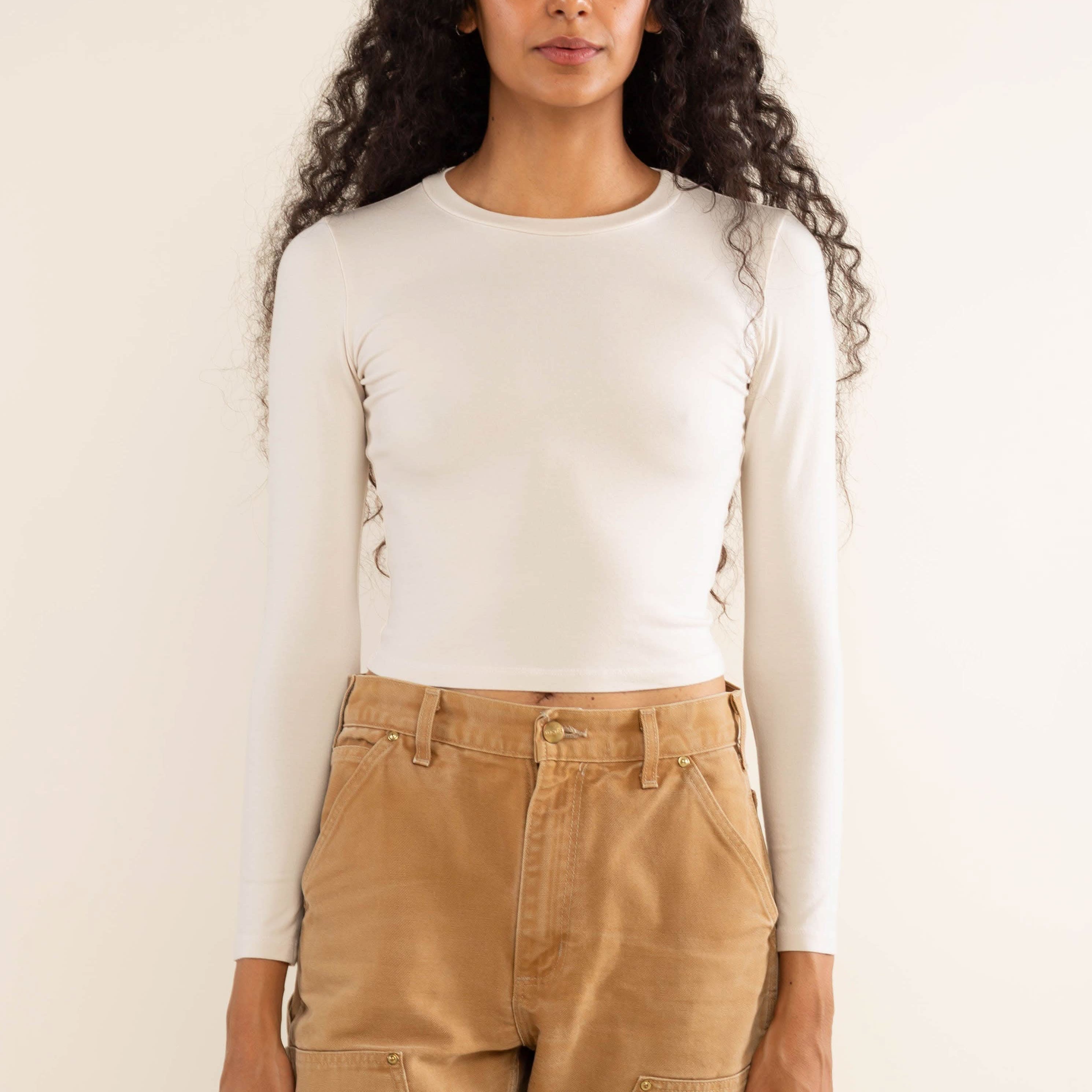Woman wearing white, long sleeve, tight, crew neck, top with khaki jeans