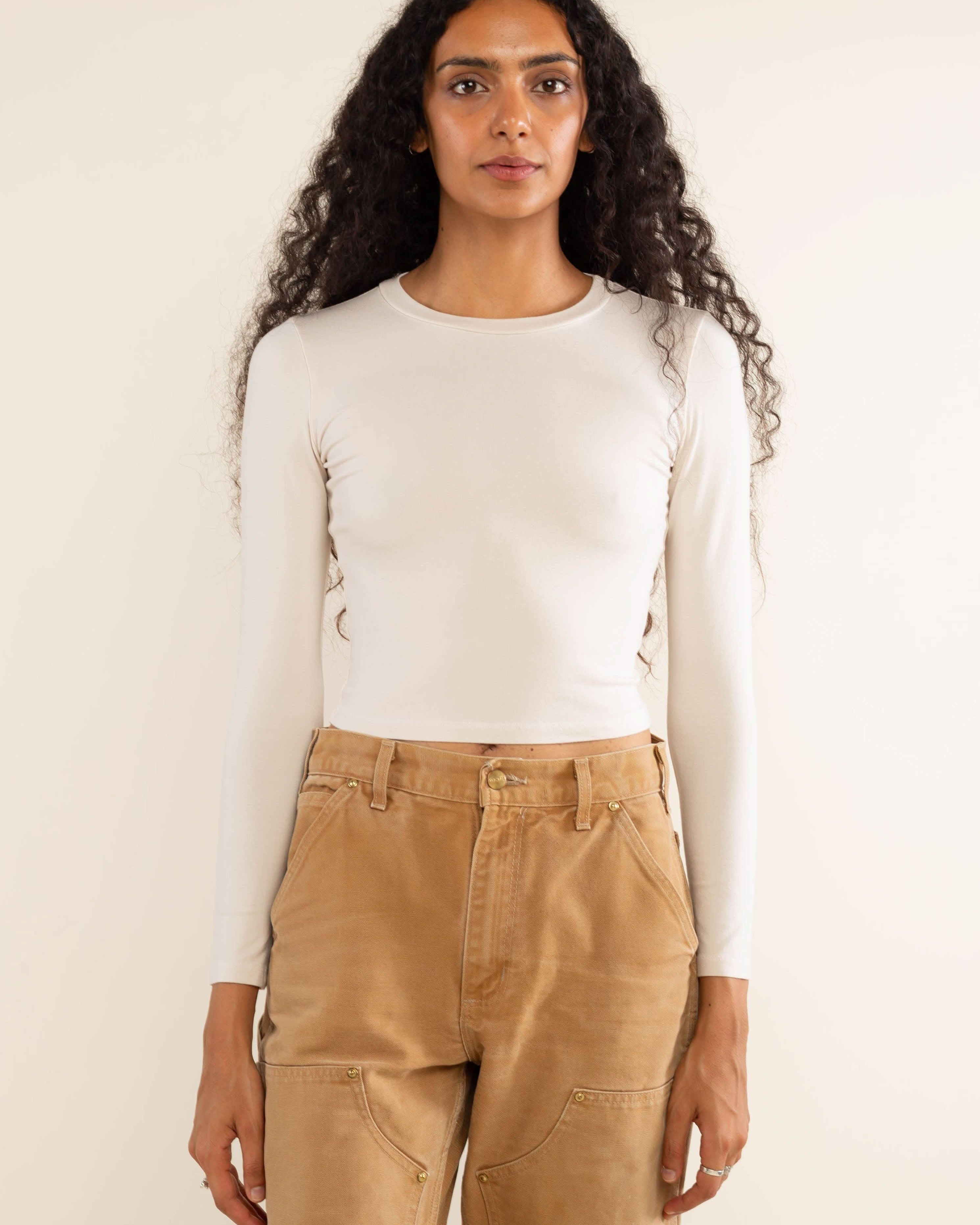 Woman wearing white, long sleeve, tight, crew neck, top with khaki jeans