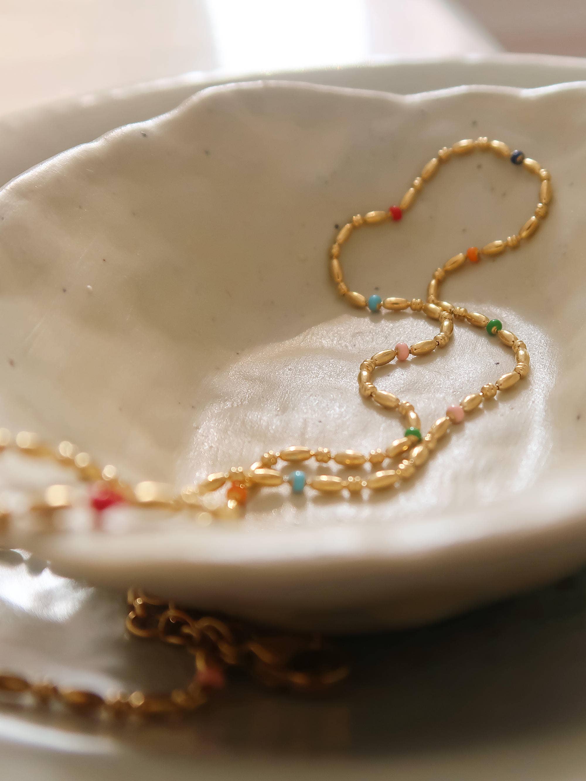 Gold necklace with colorful beads on a white dish