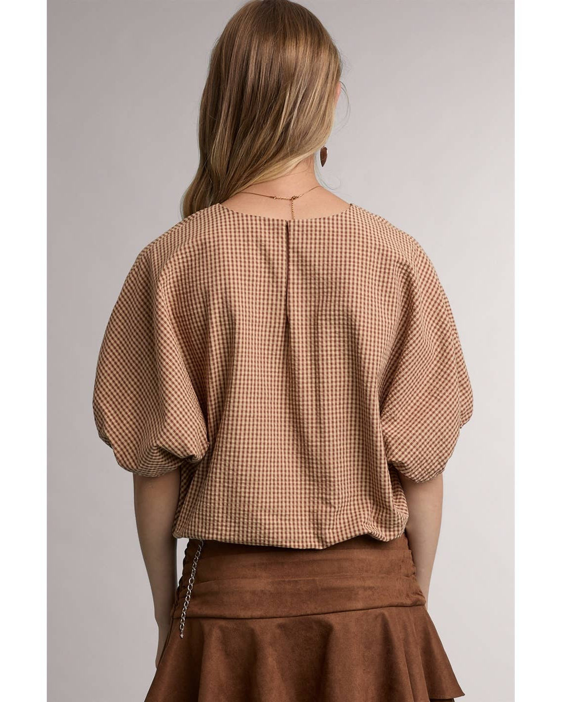 A woman shown from the back wearing a cropped short-sleeve blouse with a brown and beige gingham pattern and a brown skirt, set against a plain light gray studio background.
