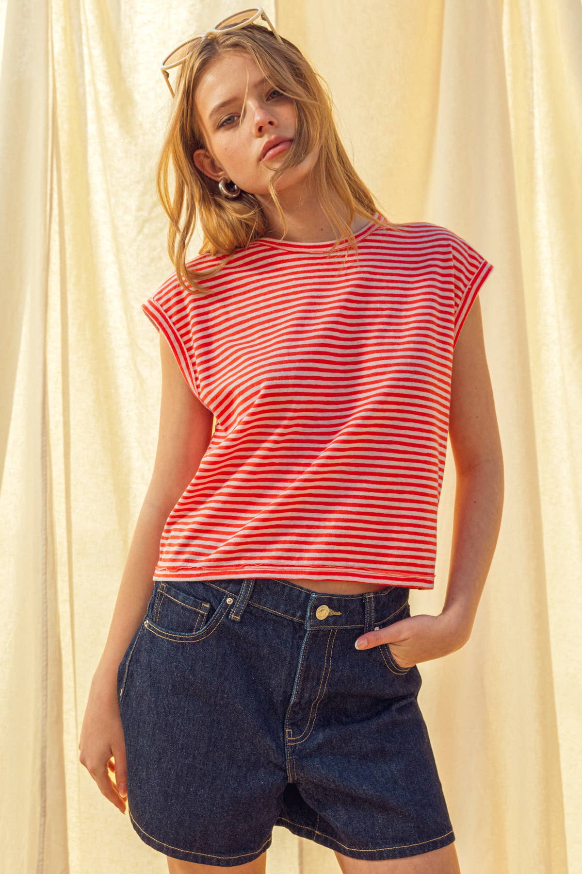 Woman wearing a red and white striped shirt with dark denim shorts against a light background
