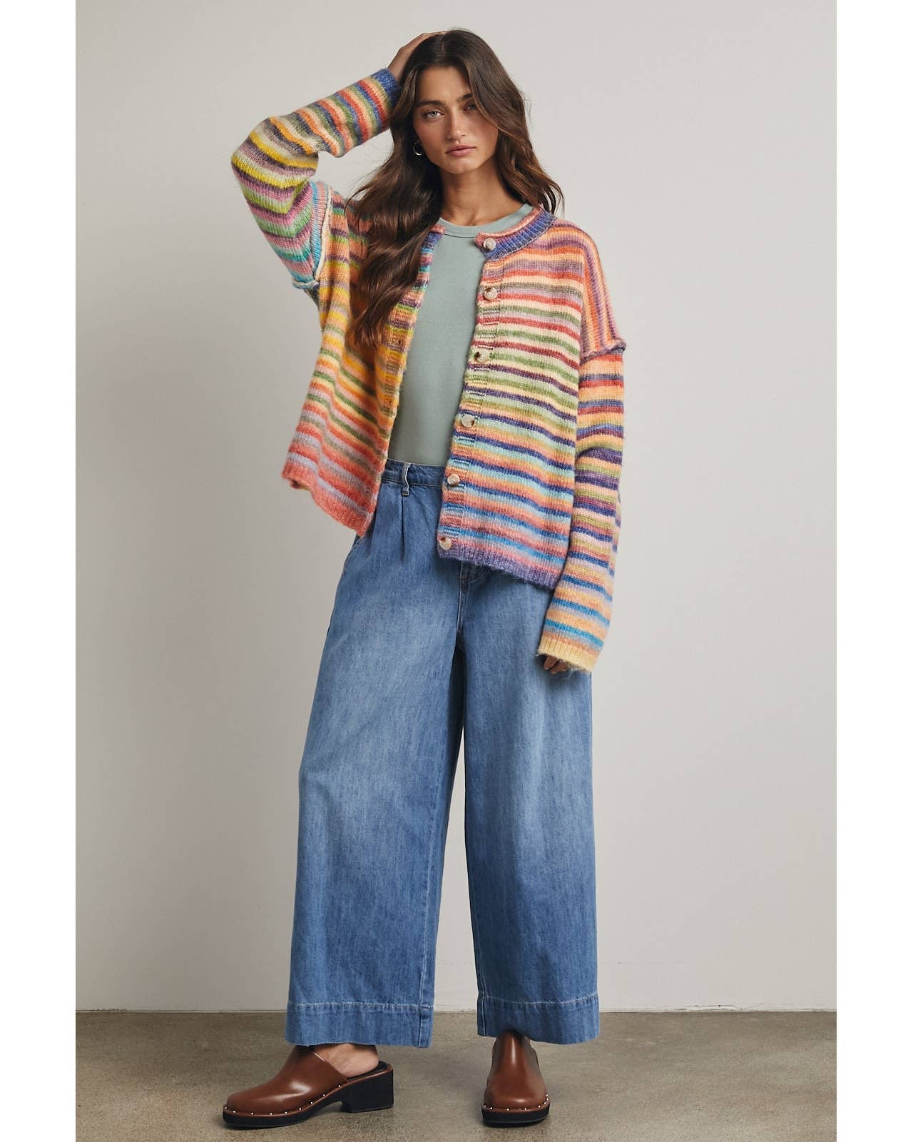 Woman wearing a colorful striped cardigan, green top, and blue jeans against a neutral background