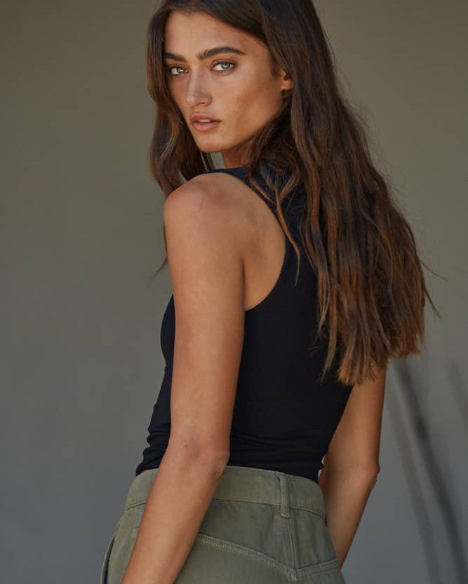 Woman wearing a black sleeveless top and green pants against a neutral background