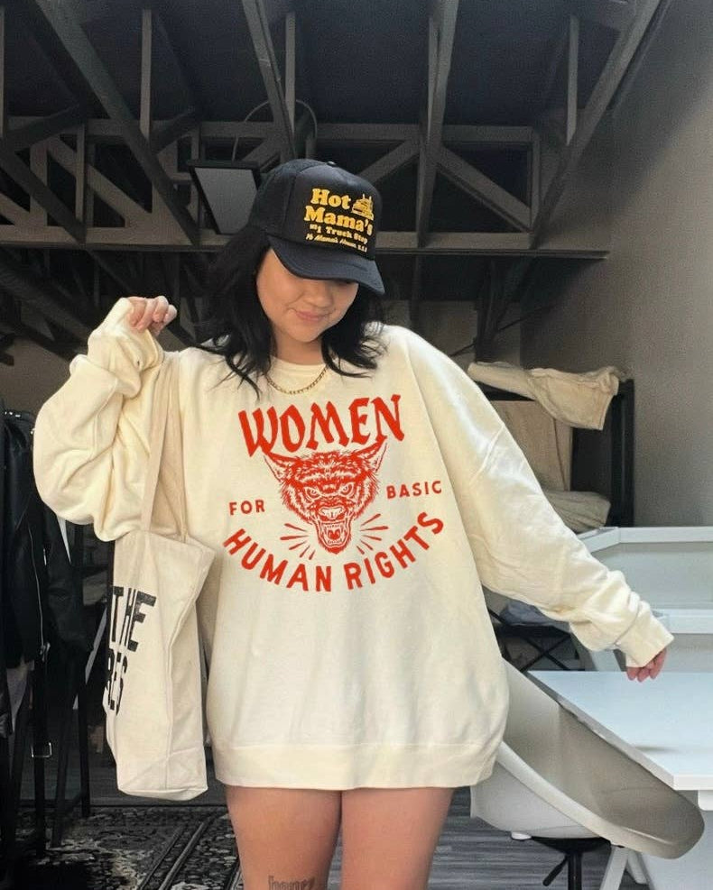 Person wearing a white sweatshirt with red text and a black cap in an indoor setting.