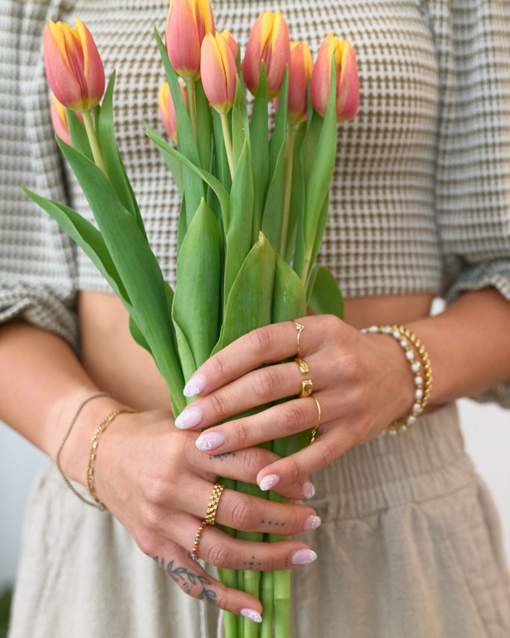 Woman holding flower and many rings including Gold, waterproof, tarnish free, watch band ring on a white background