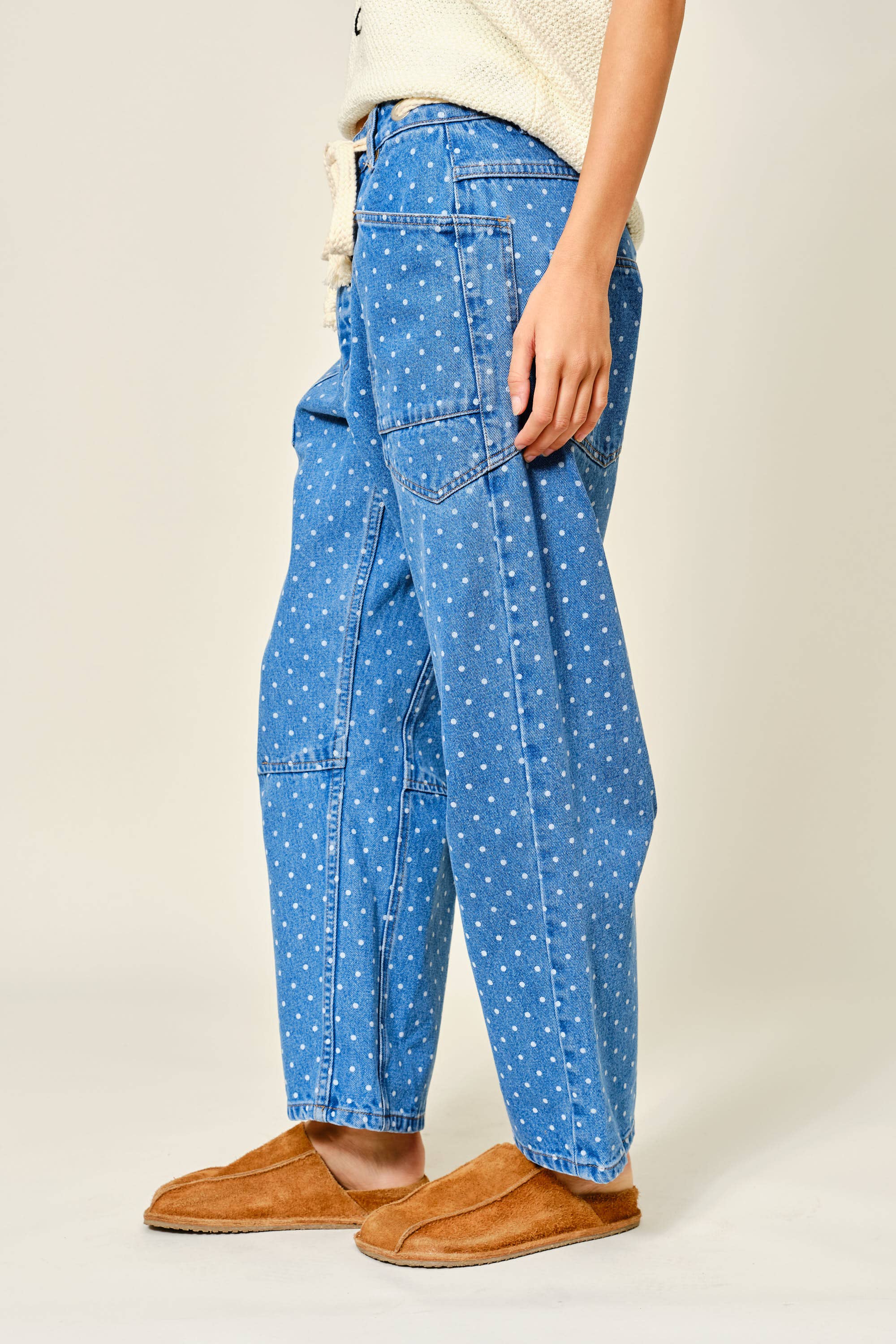 Person wearing blue polka dot pants and brown slippers on a plain background