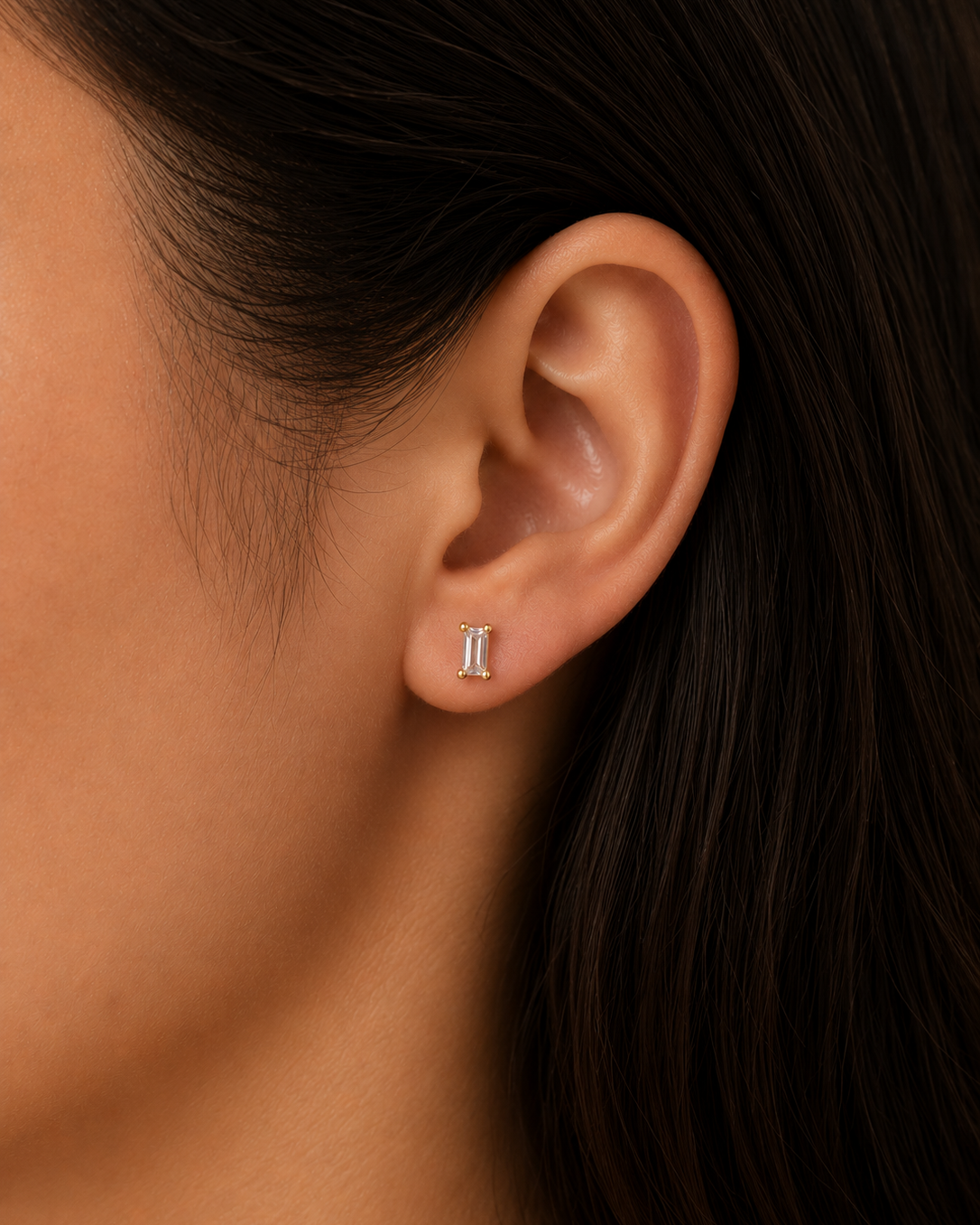 Close-up of an ear wearing a small earring with dark hair and skin background