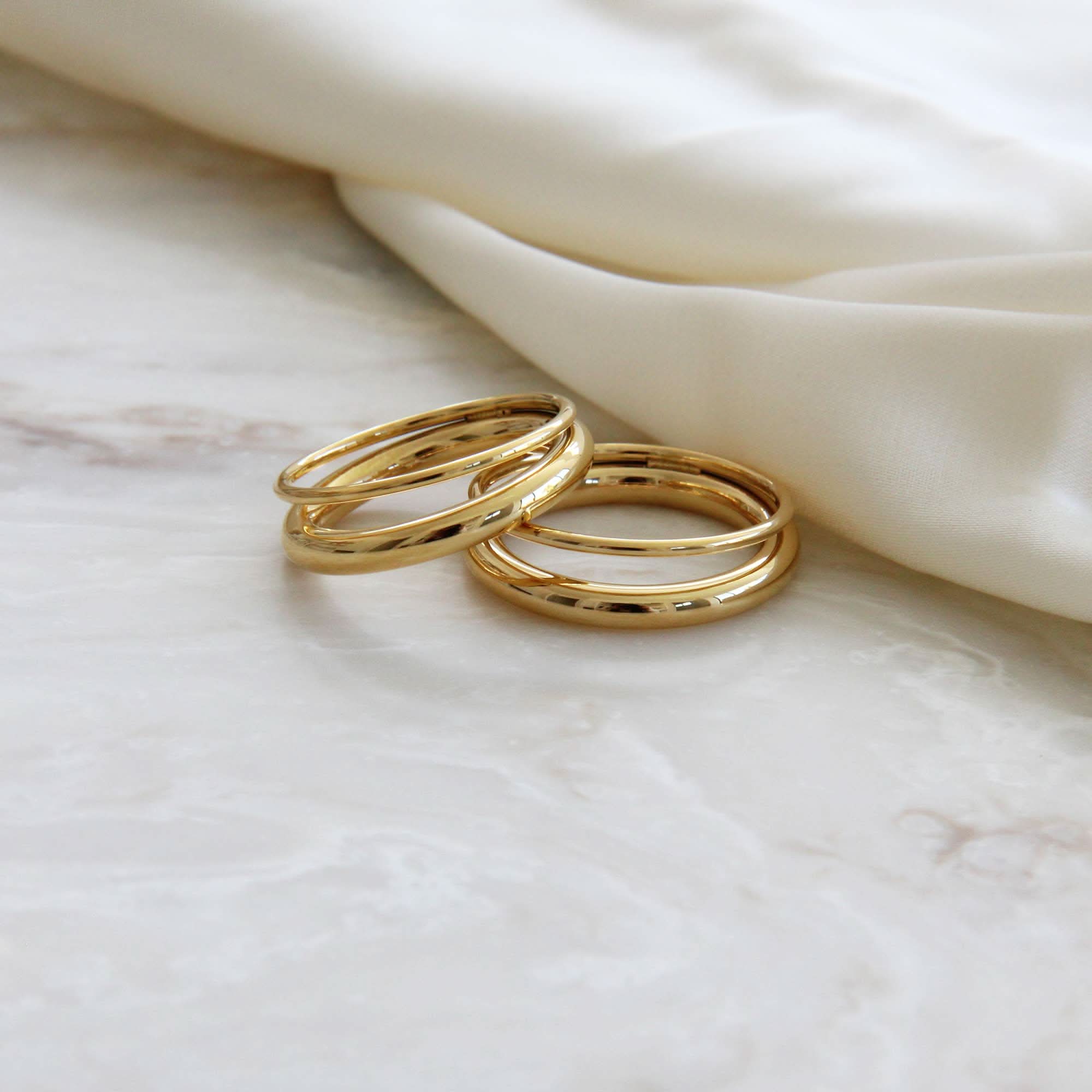 Two gold rings on a marble surface with a soft fabric background