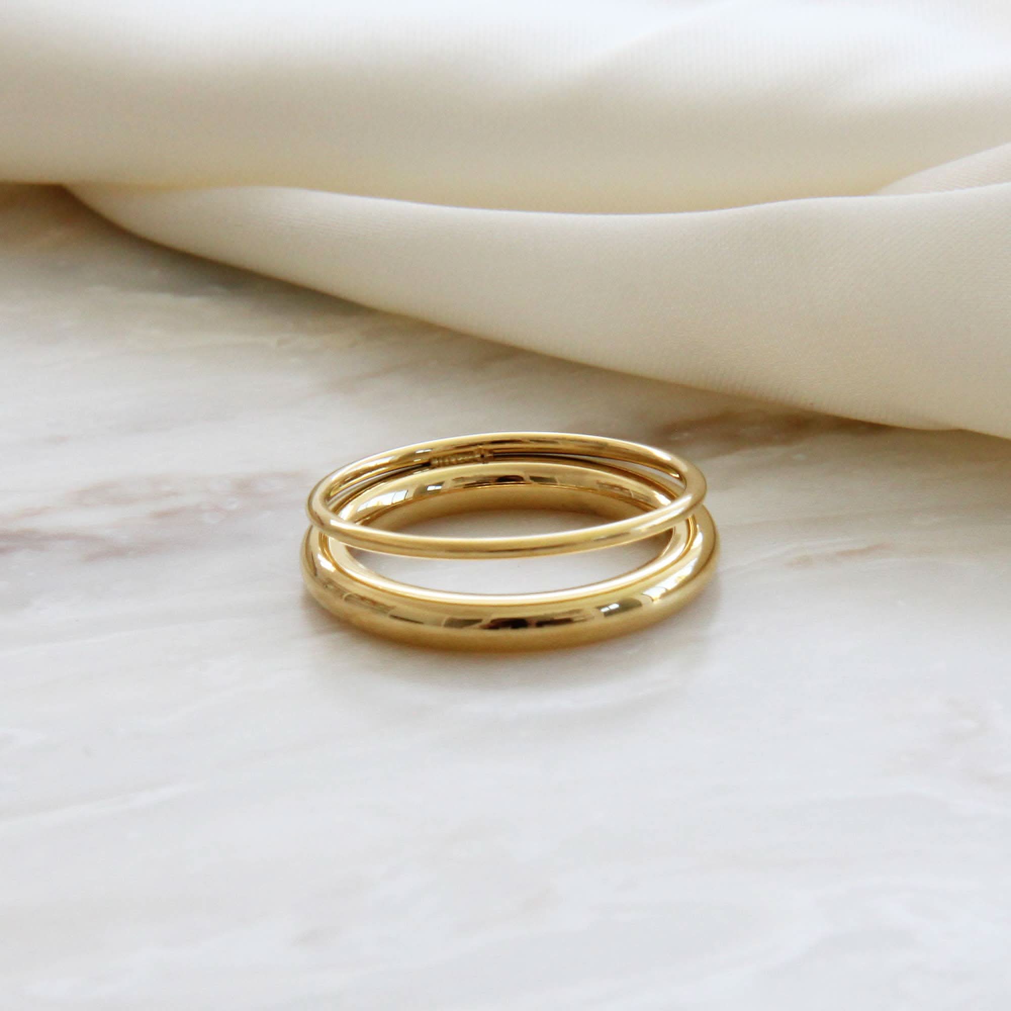 Two gold rings stacked on a marble surface with a soft beige fabric