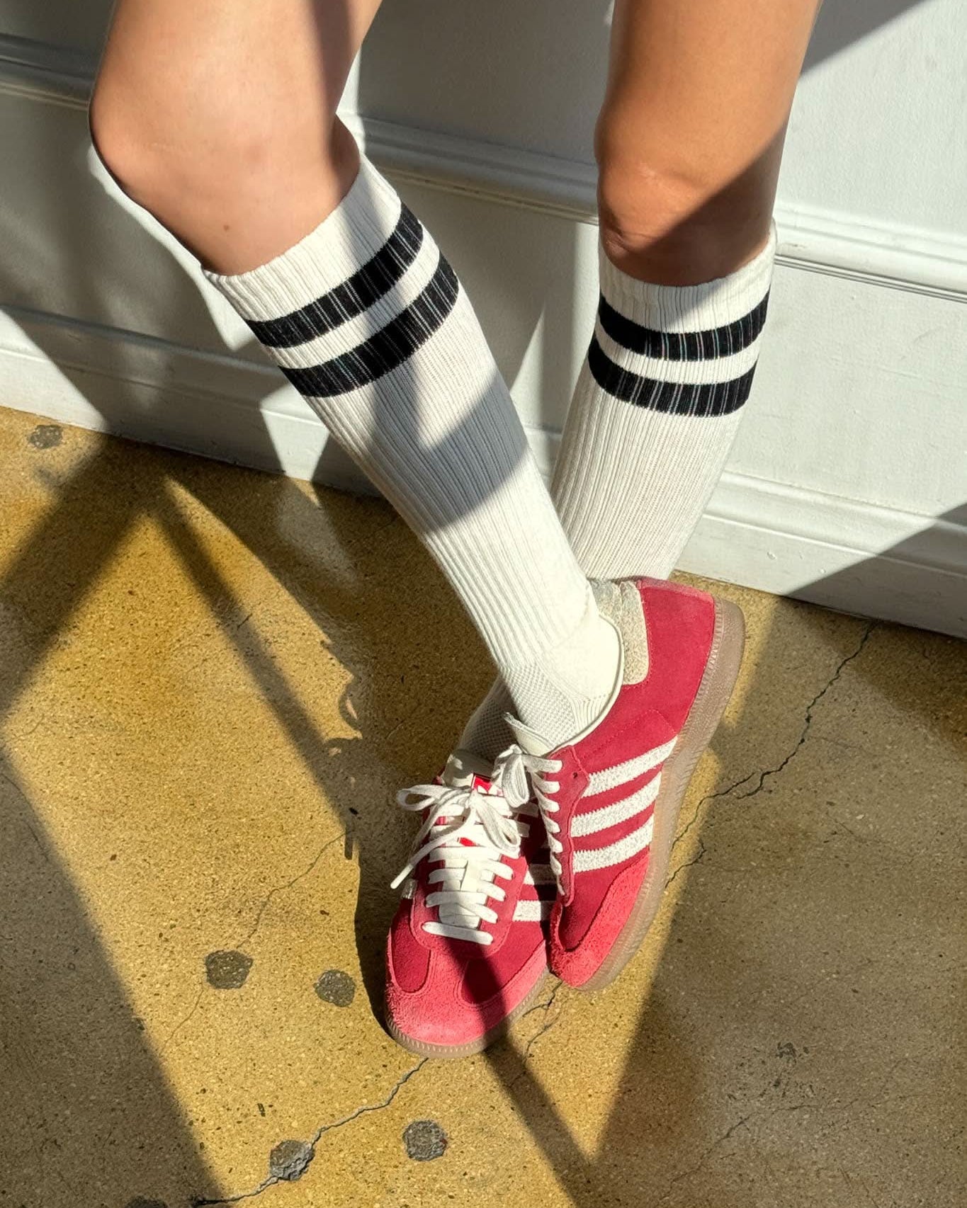 Person wearing red Adidas sneakers and white socks with black stripes on a concrete floor.