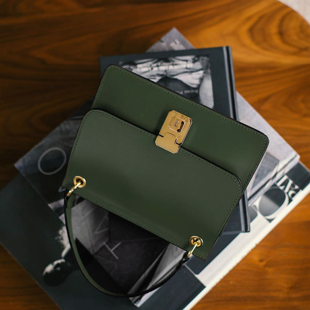 Green handbag with gold accents on a stack of books on a wooden surface