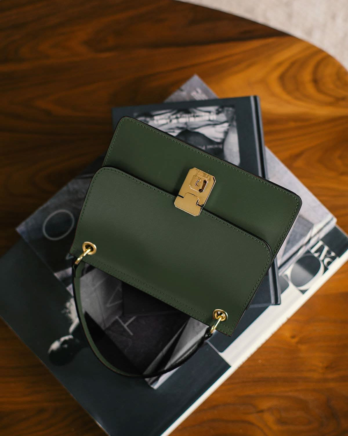 Green handbag with gold accents on a stack of books on a wooden surface