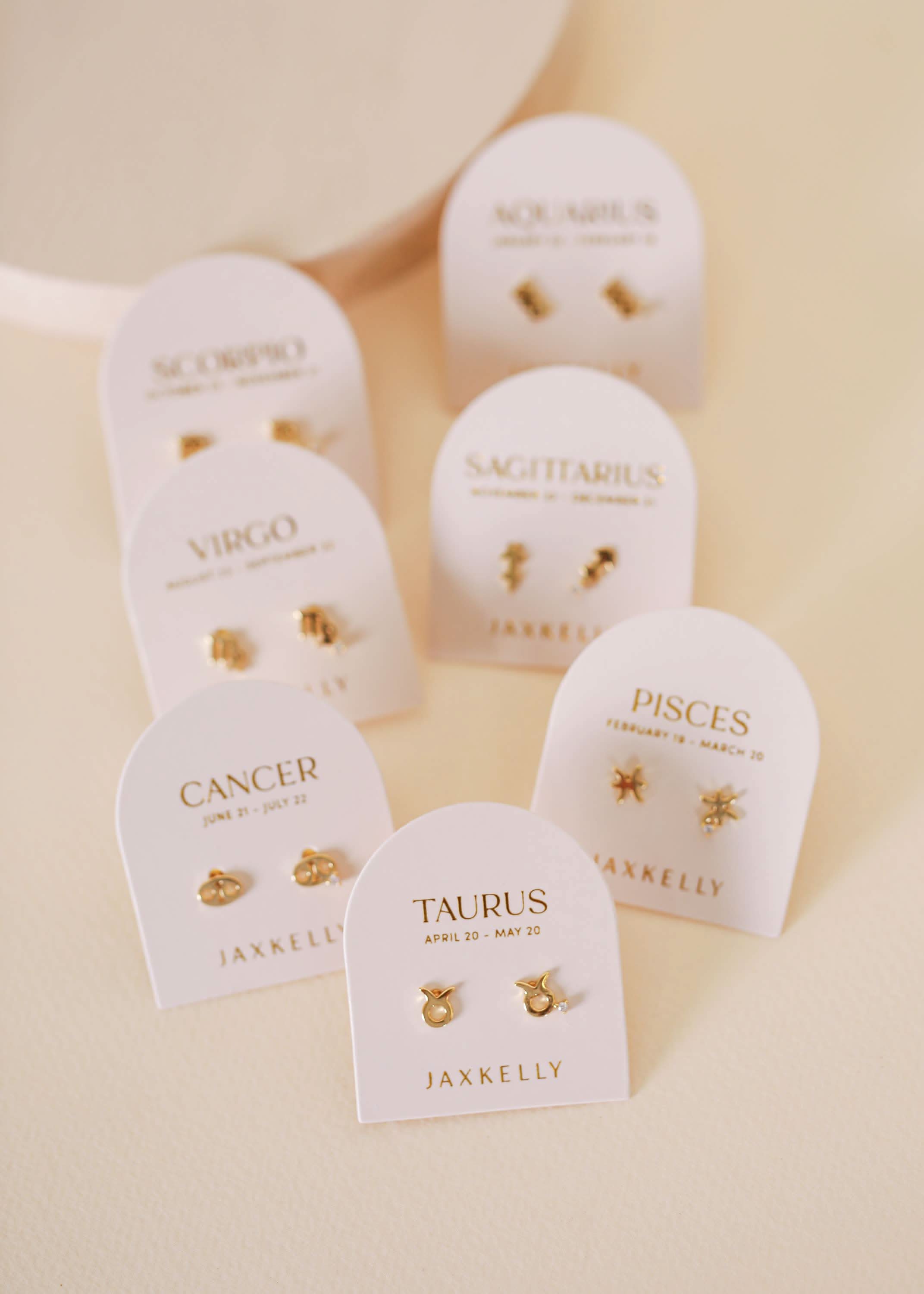 Gold zodiac charm studs in the shape of Aquarius, Taurus, Pisces, Virgo, Scorpio and Aquarius astrological signs. Each displayed on earring card a separate earring card