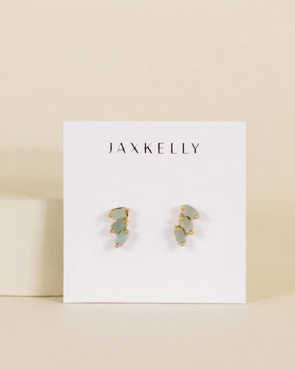 Pair of earrings on a Jaxkelly branded card against a beige background